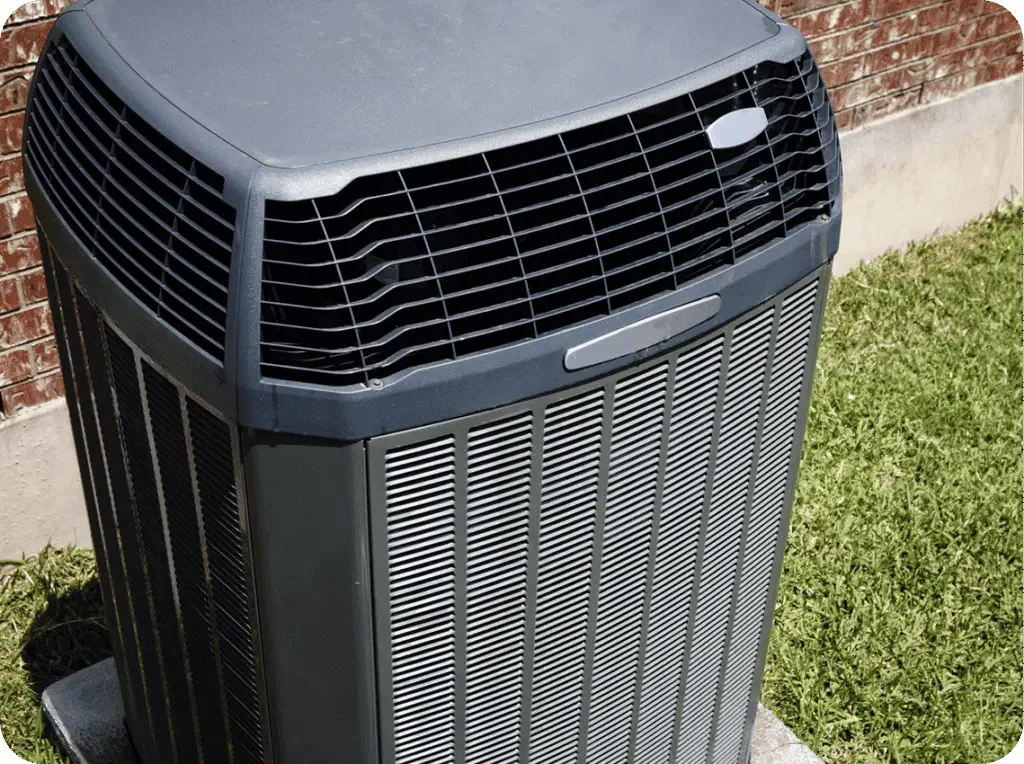 Outdoor air conditioning unit beside brick wall and grass.