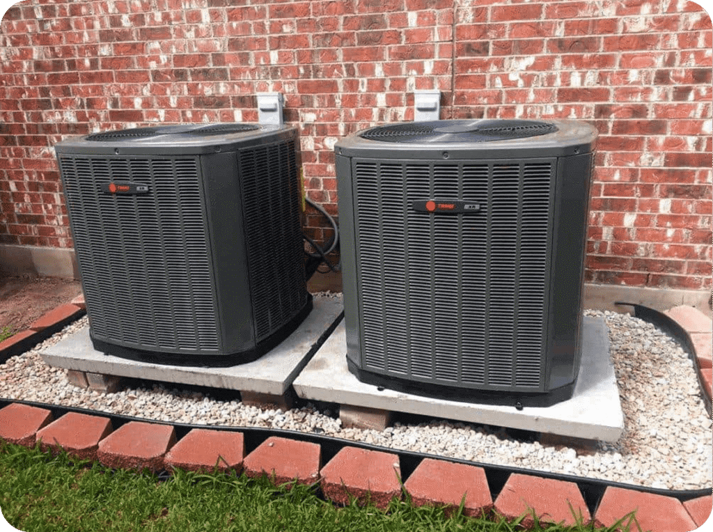 Two Trane air conditioning units on concrete pads outside a brick building, surrounded by gravel and a brick border.