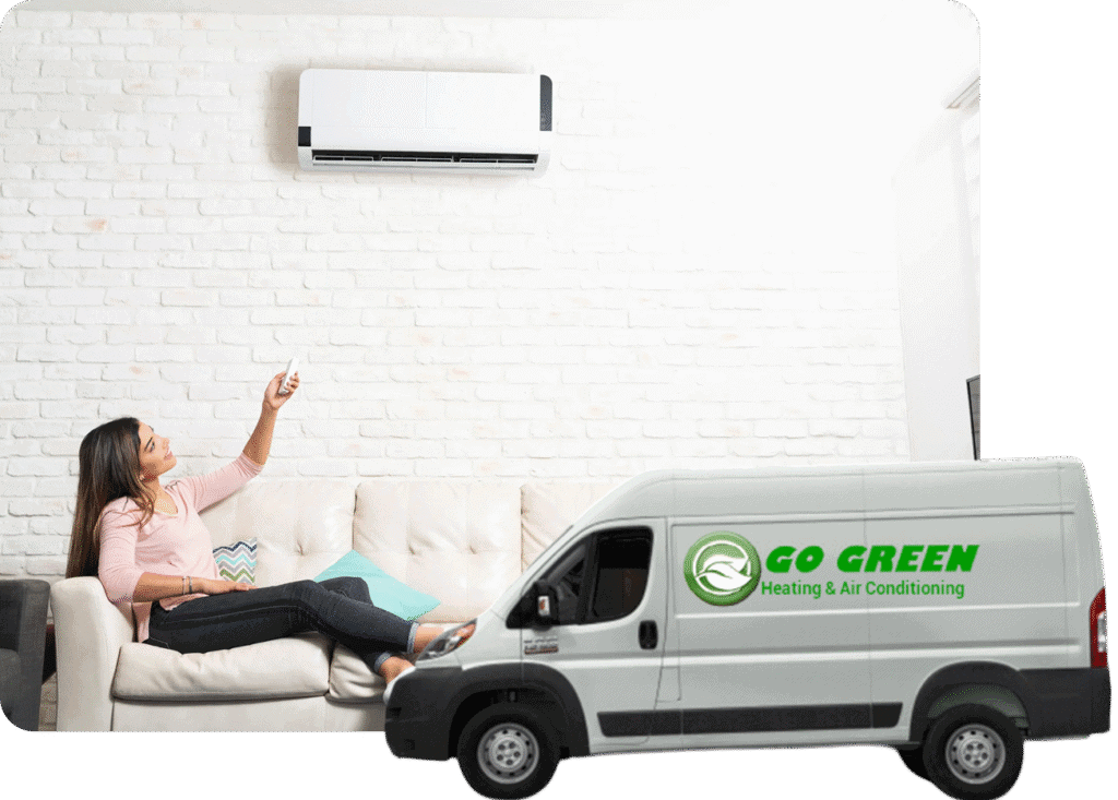 A woman sitting on a white couch in a modern room with a brick wall, taking a selfie or video with a smartphone. An air conditioning unit is mounted on the wall above her, and a white van with green text that reads 'GO GREEN Heating & Air Conditioning' is parked indoors near her.