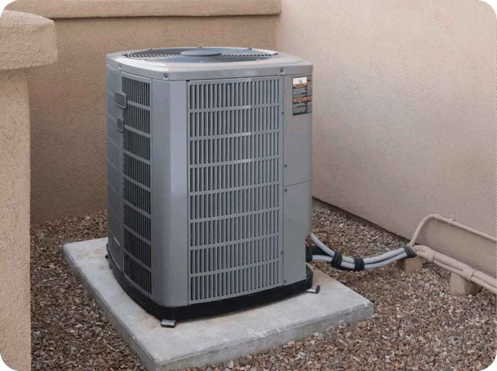 An outdoor air conditioning unit placed on a concrete slab against beige walls.