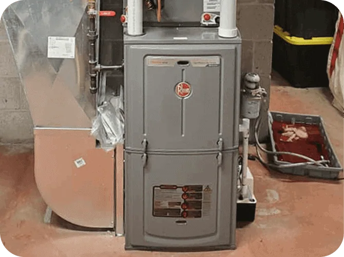 A utility furnace in a basement with pipes and a metal vent duct.