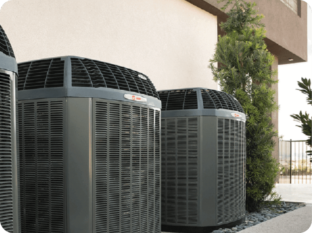 Two large outdoor air conditioning units next to a building with a tree to the right.