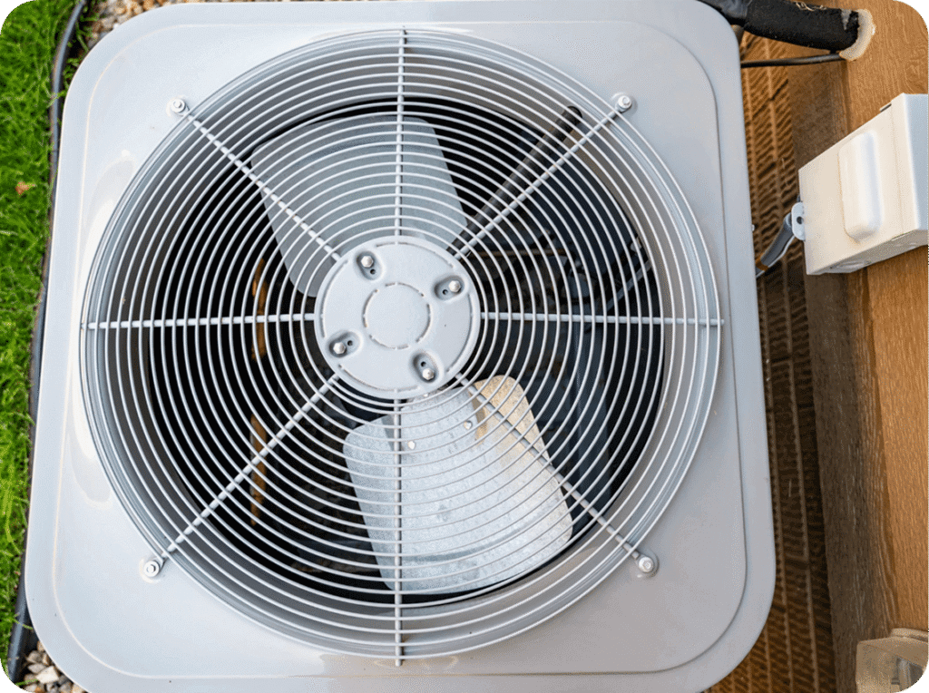 Top view of an air conditioning unit outdoor compressor with a protective grill on top and a wooden deck beside it.