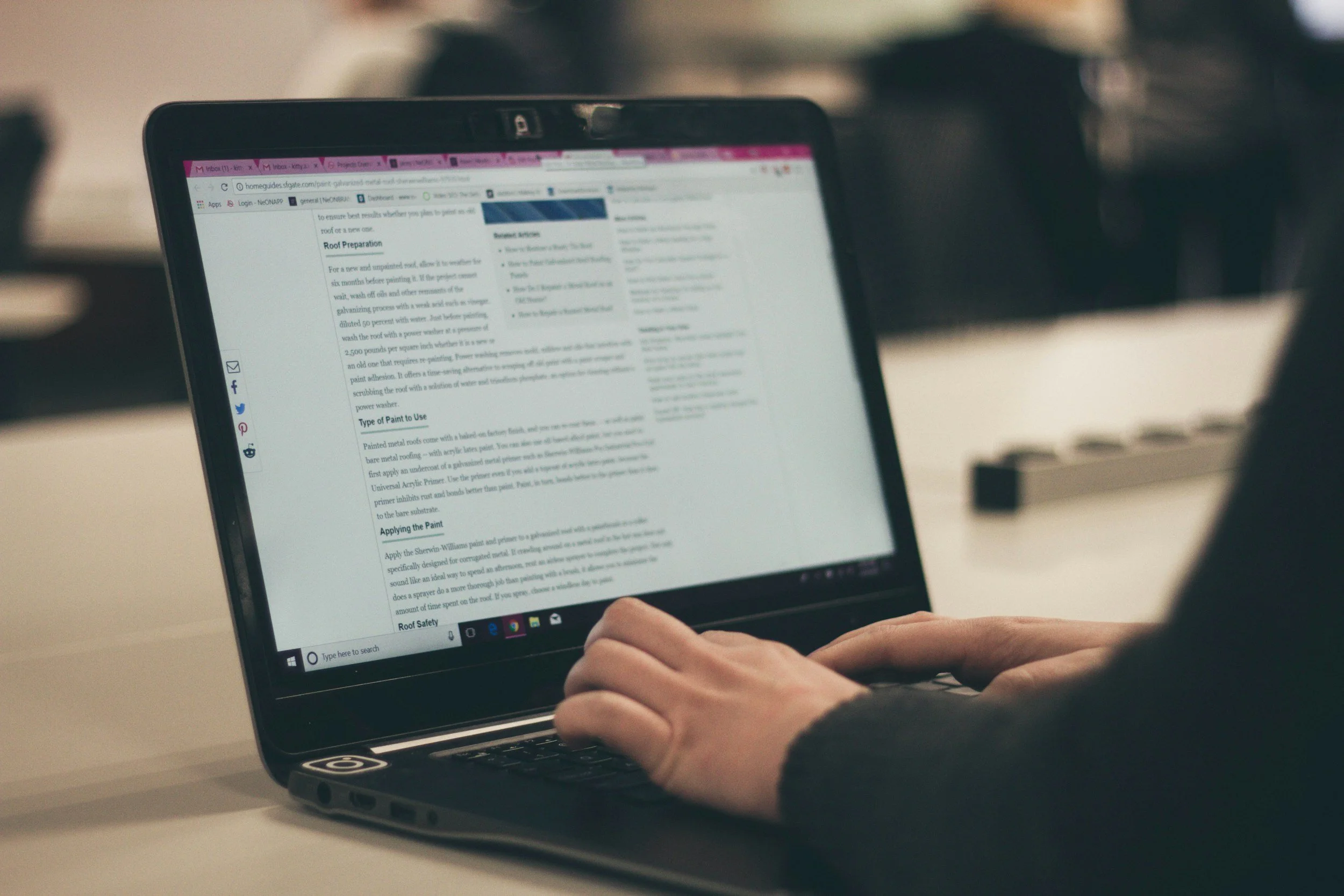 AI to write a blog. Person holding a tablet displaying a webpage about roof preparation and paint application, with a blurred background.
