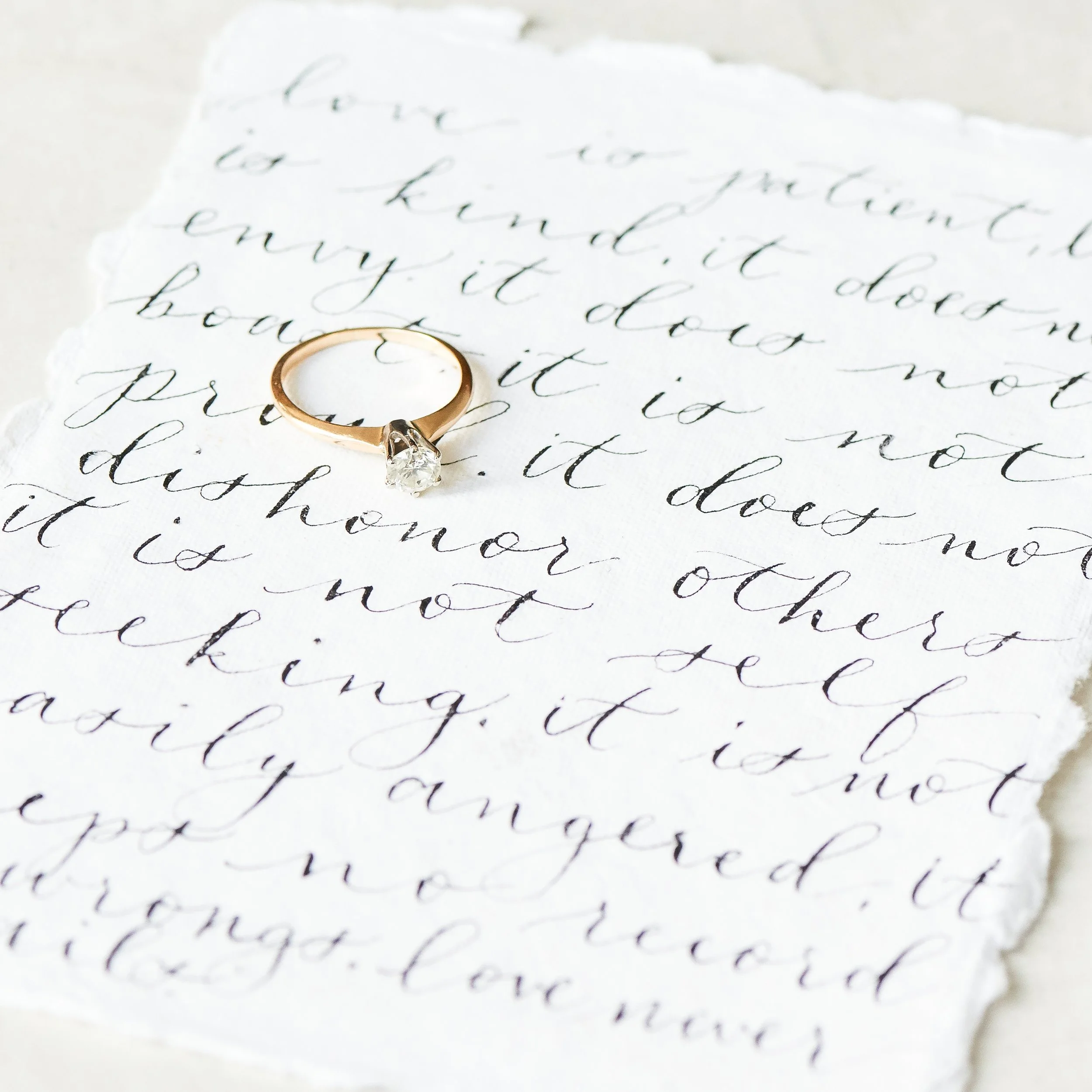 Close-up of handwritten letter with a gold ring placed on it, written in black cursive ink on white paper.