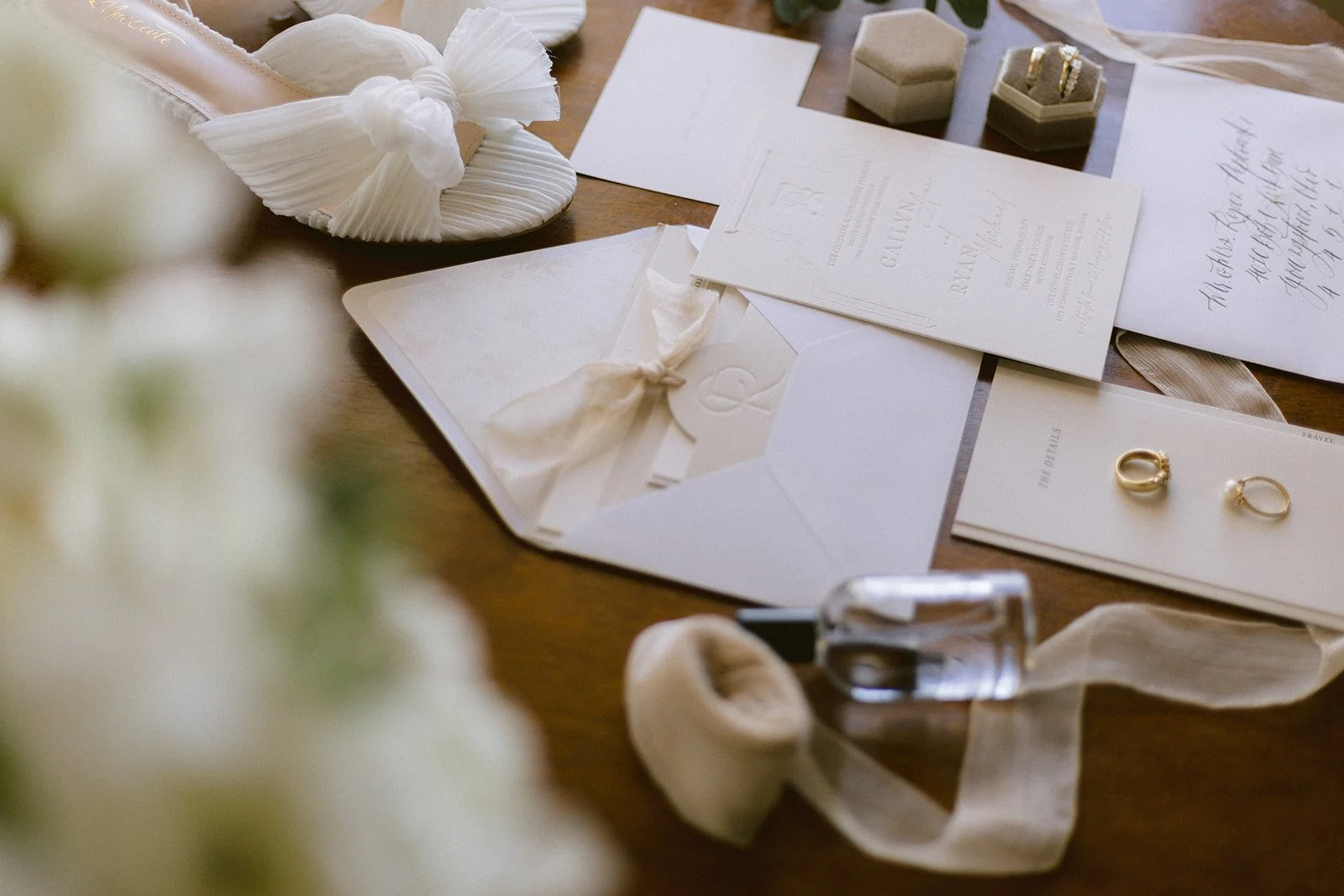 Wedding invitation suite featuring white envelopes, rings, and small decorative boxes on a wooden table.
