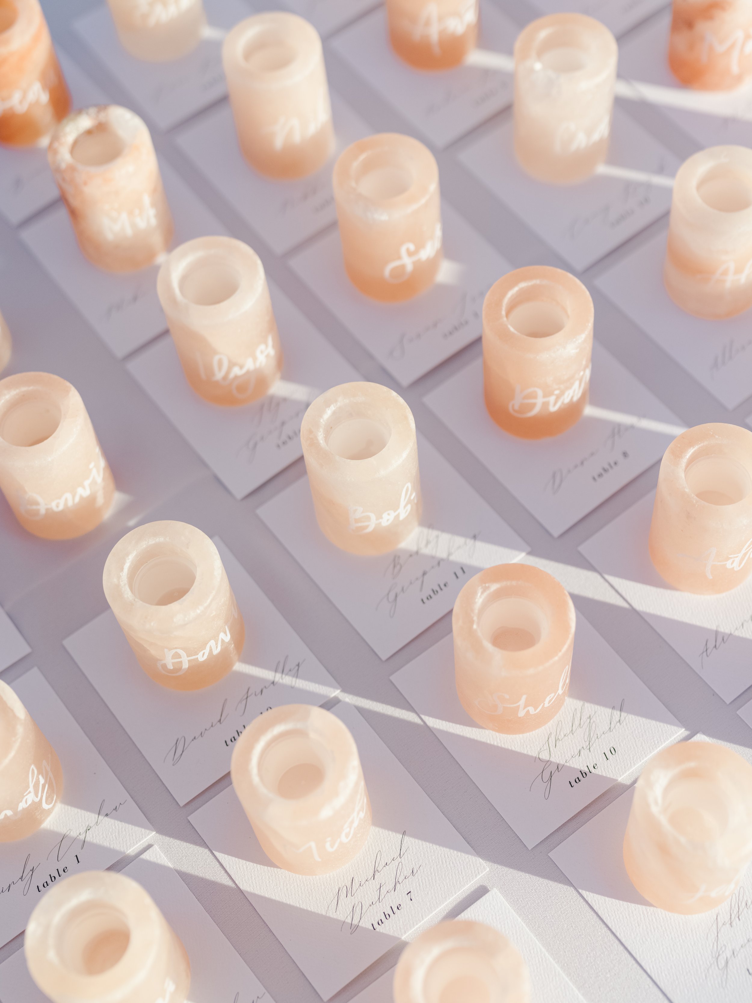 Multiple peach-colored shot glasses and place cards with handwritten names arranged on a table.