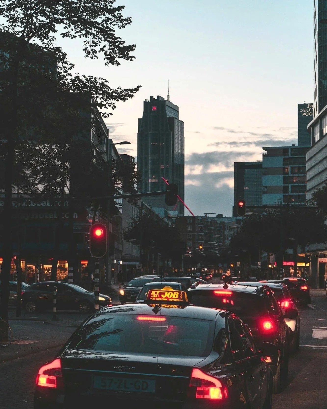 Straatbeeld in een stad met autorijver, verkeerslichten en hoge gebouwen bij zonsondergang.