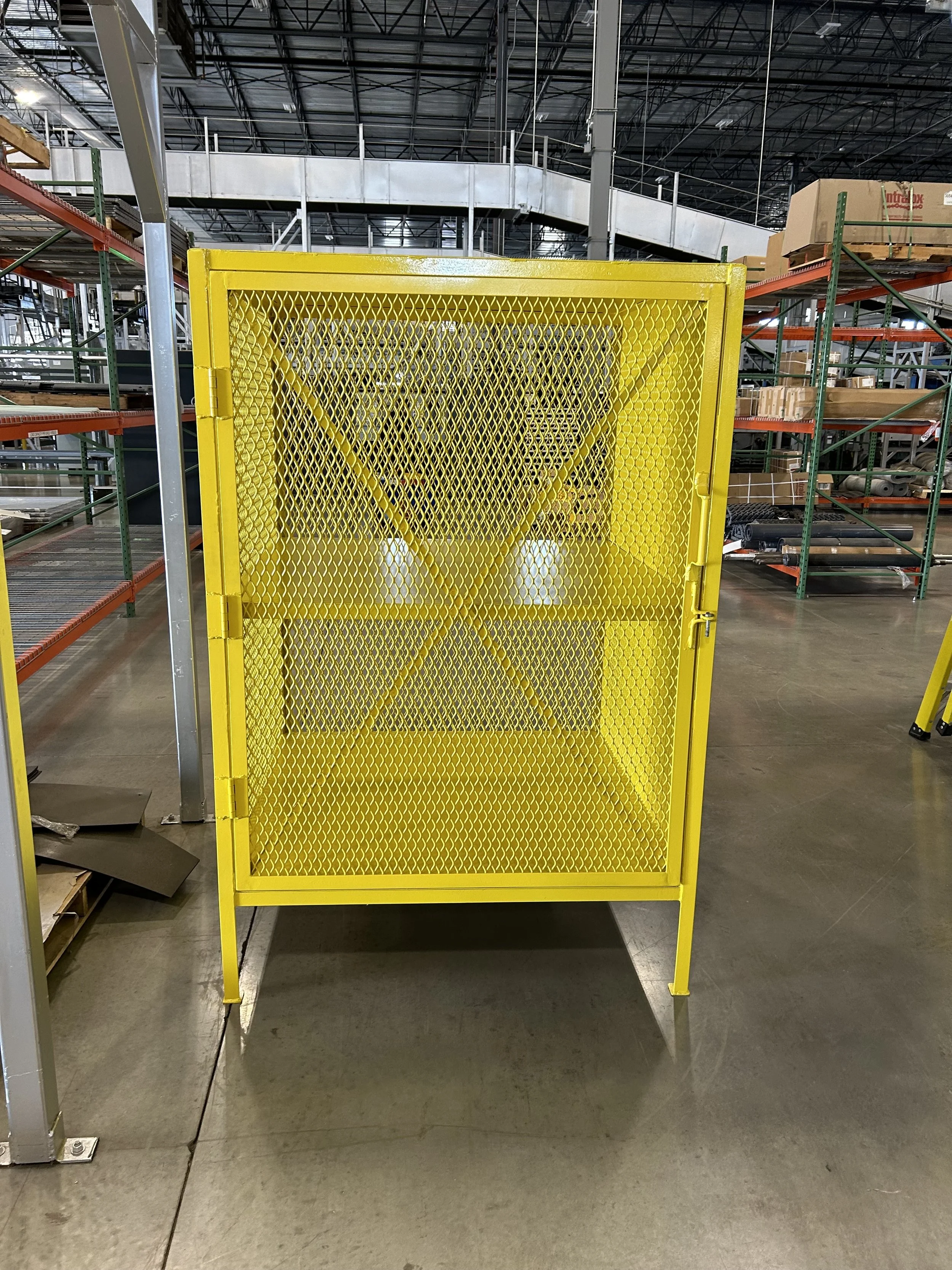 A yellow safety barrier in a warehouse, with shelving and boxes in the background.