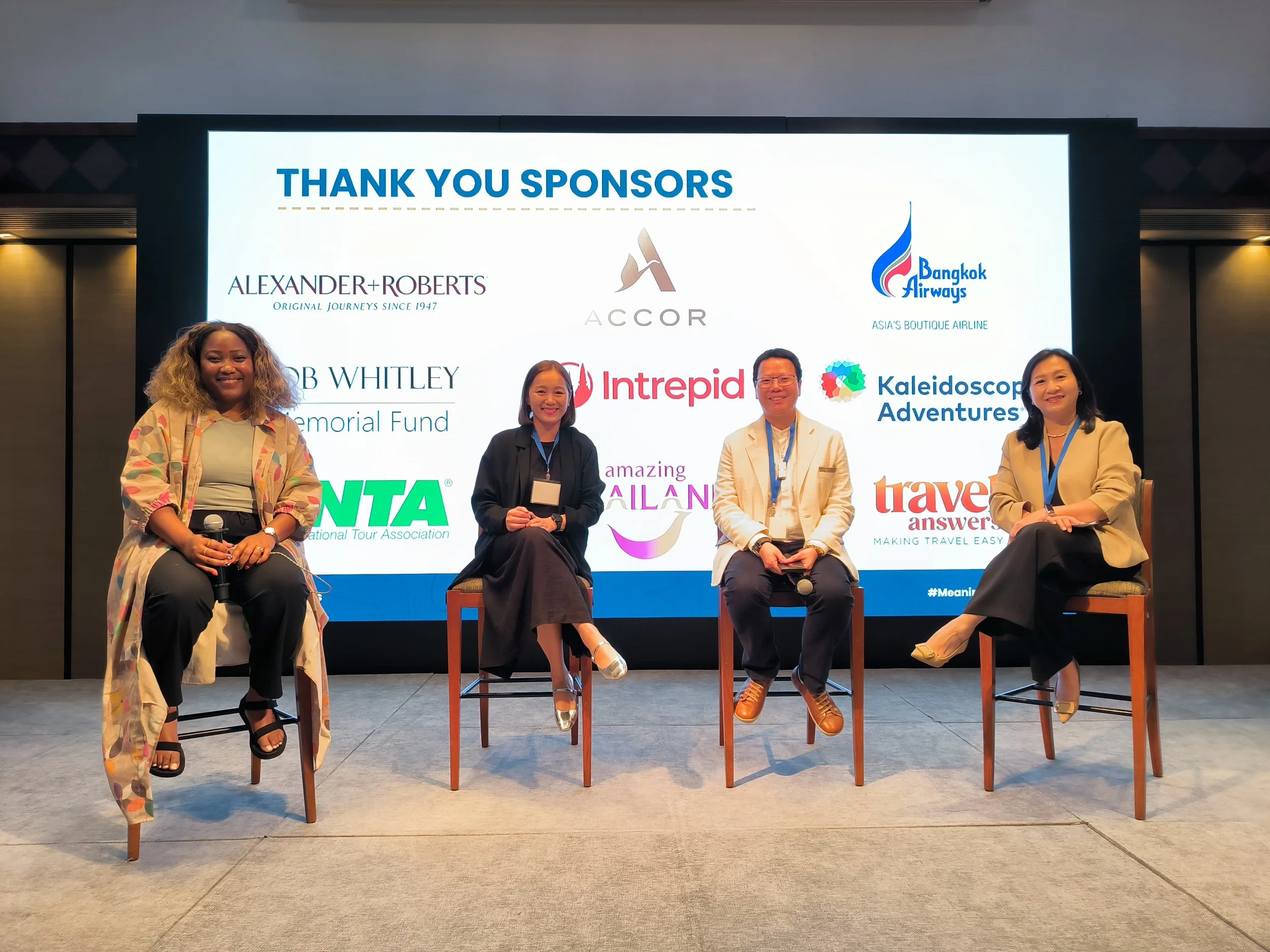 Four people sitting on chairs in front of a large screen displaying sponsor logos at a conference or event. The screen reads "Thank You Sponsors" and features logos for Alexander + Roberts, Accor, Bangkok Airways, and several others.