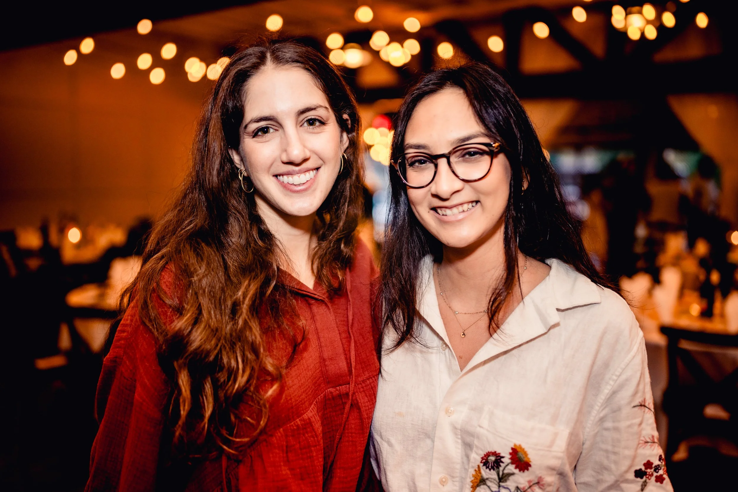 Two women smiling at a social event with warm lighting and blurred background.