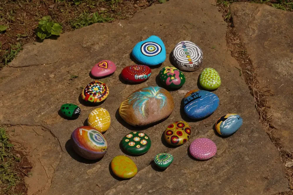 Painted rocks with various colors, patterns, and designs arranged on a stone outdoor surface.