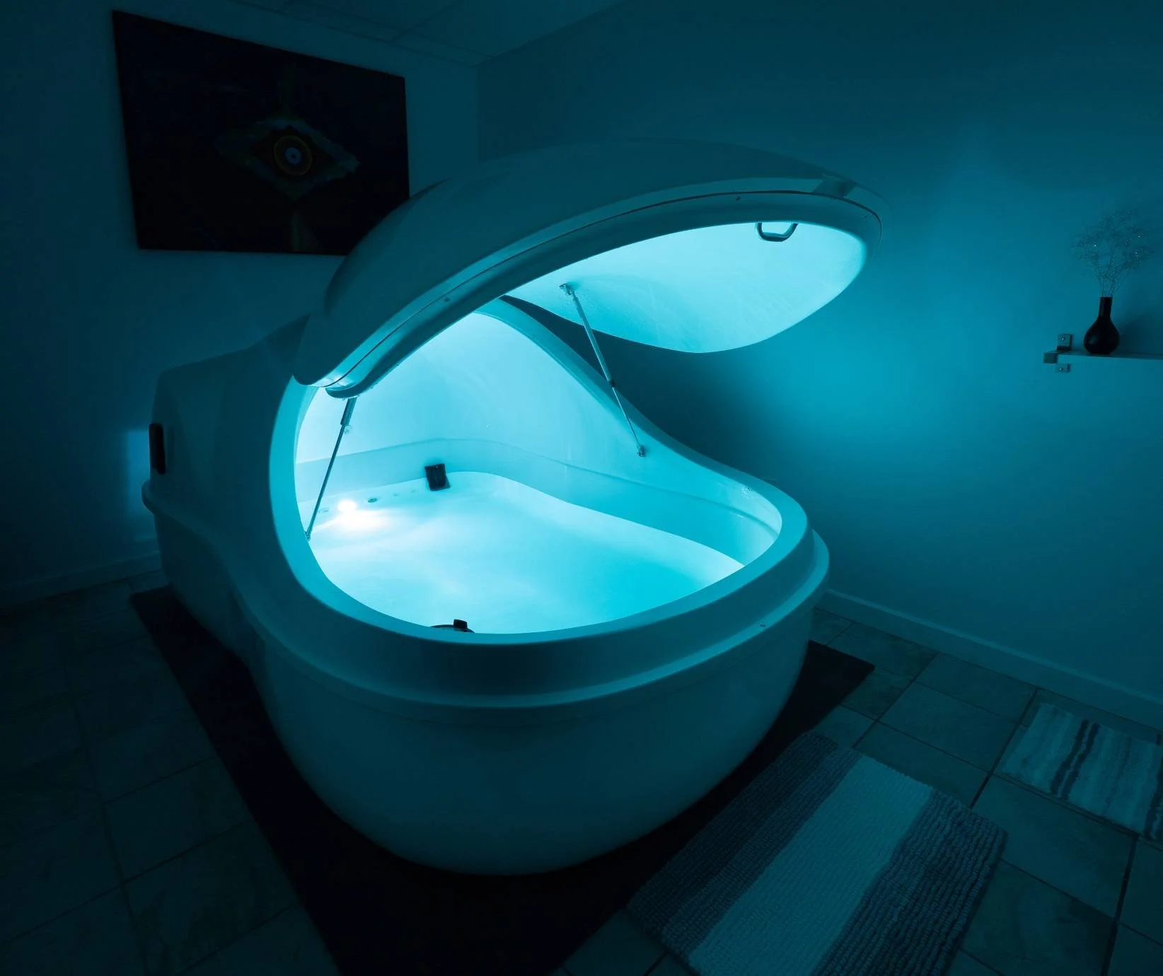 An open, modern tanning bed in a room with tiled floor and wall art, lit with blue light.