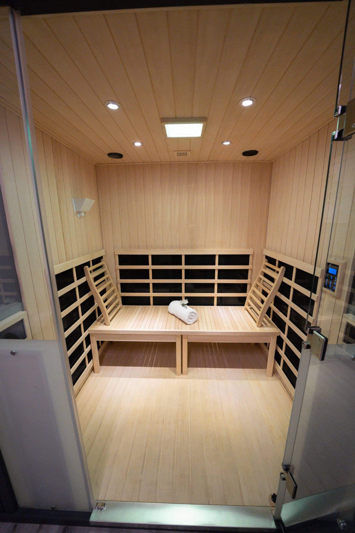 A wooden sauna interior with seating, a towel, and overhead lighting.
