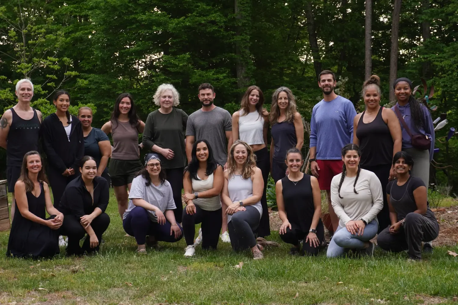 Group of women standing and kneeling outdoors in a forested area, smiling at the camera.