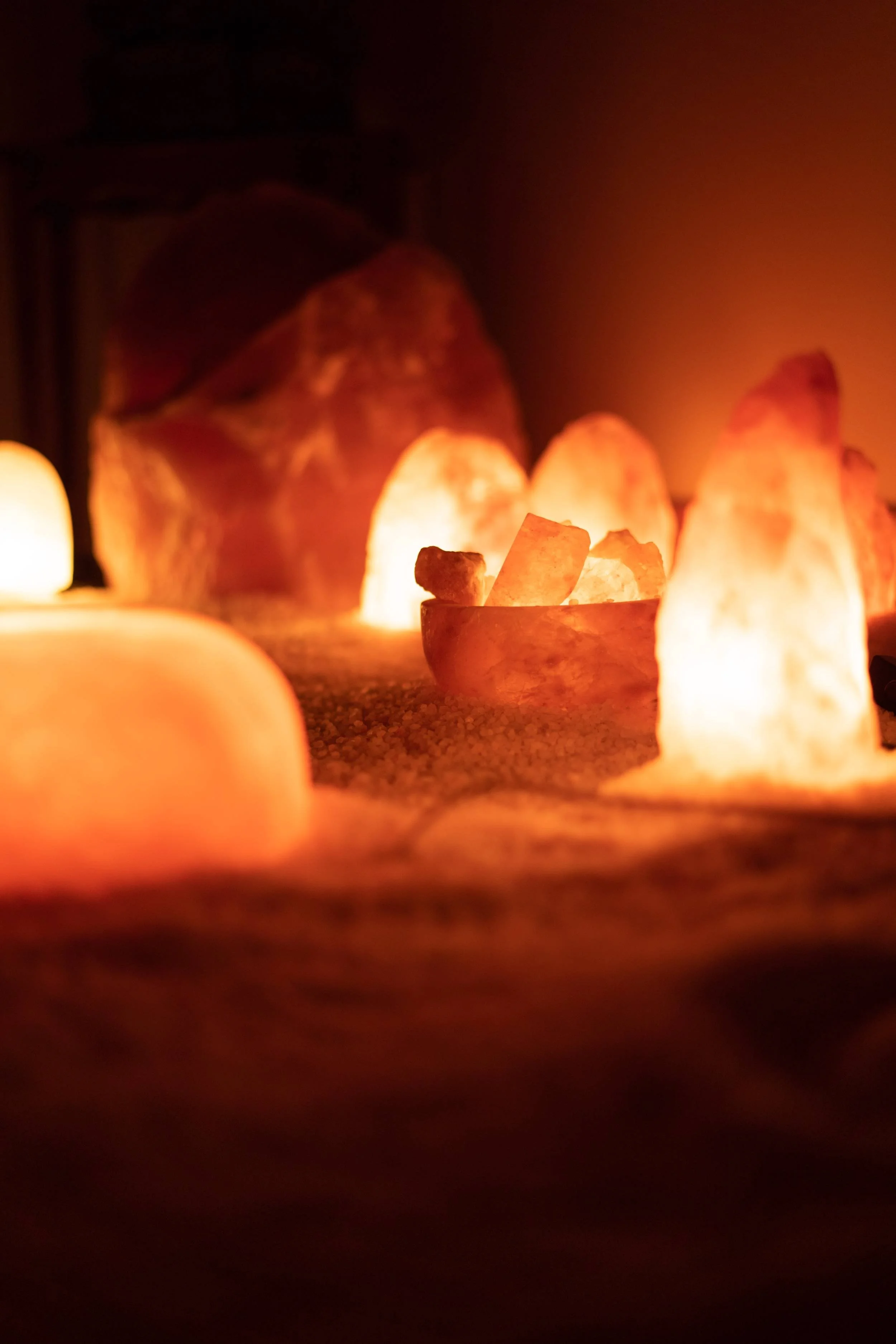 A collection of glowing salt lamps or Himalayan salt rocks emitting warm orange and pinkish light, arranged on a surface in a dimly lit room.