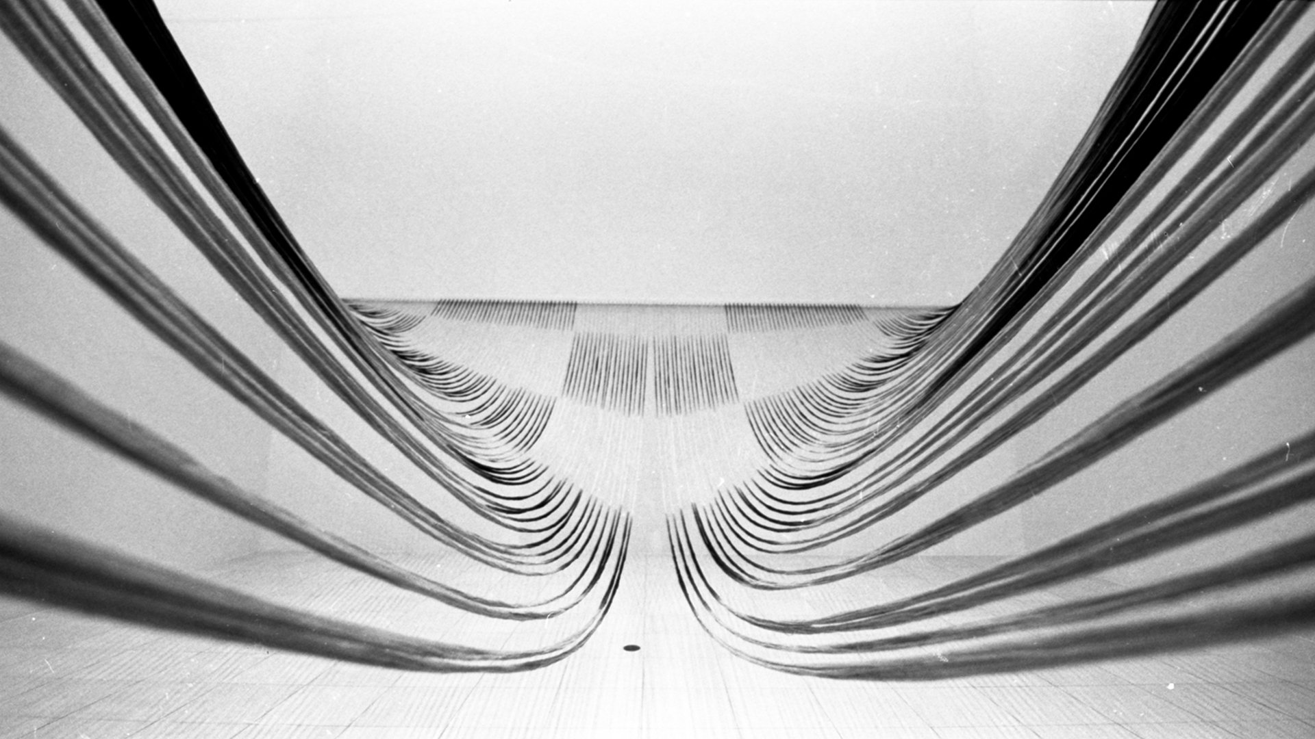 Close-up view of metallic louvers or slats arranged in a square frame, creating a symmetrical pattern. The photo is in black and white.