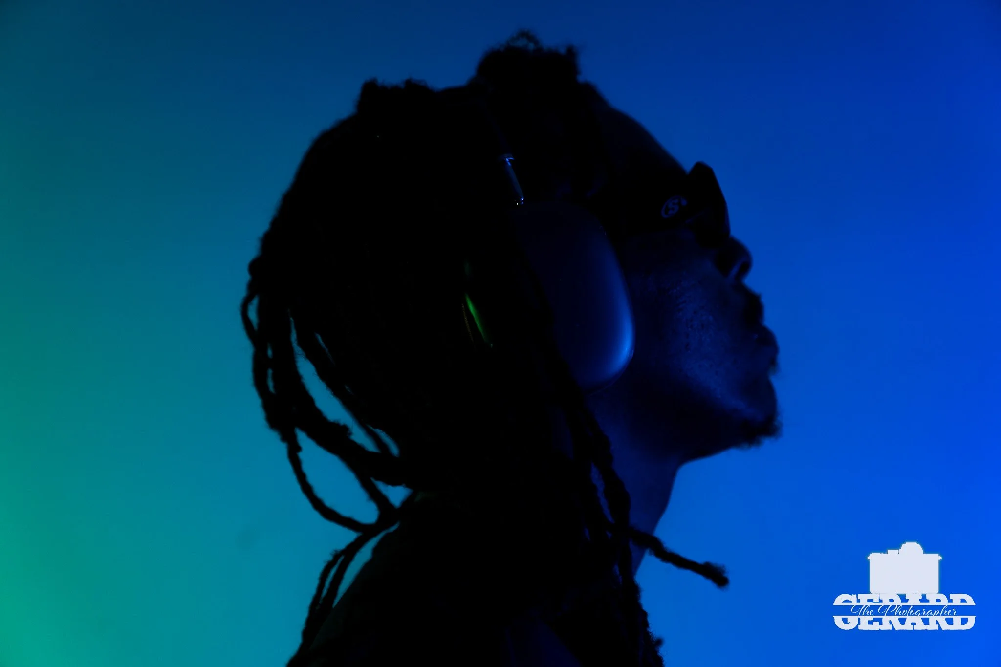 Silhouette of a person with glasses and dreadlocks against a gradient blue background, wearing headphones.