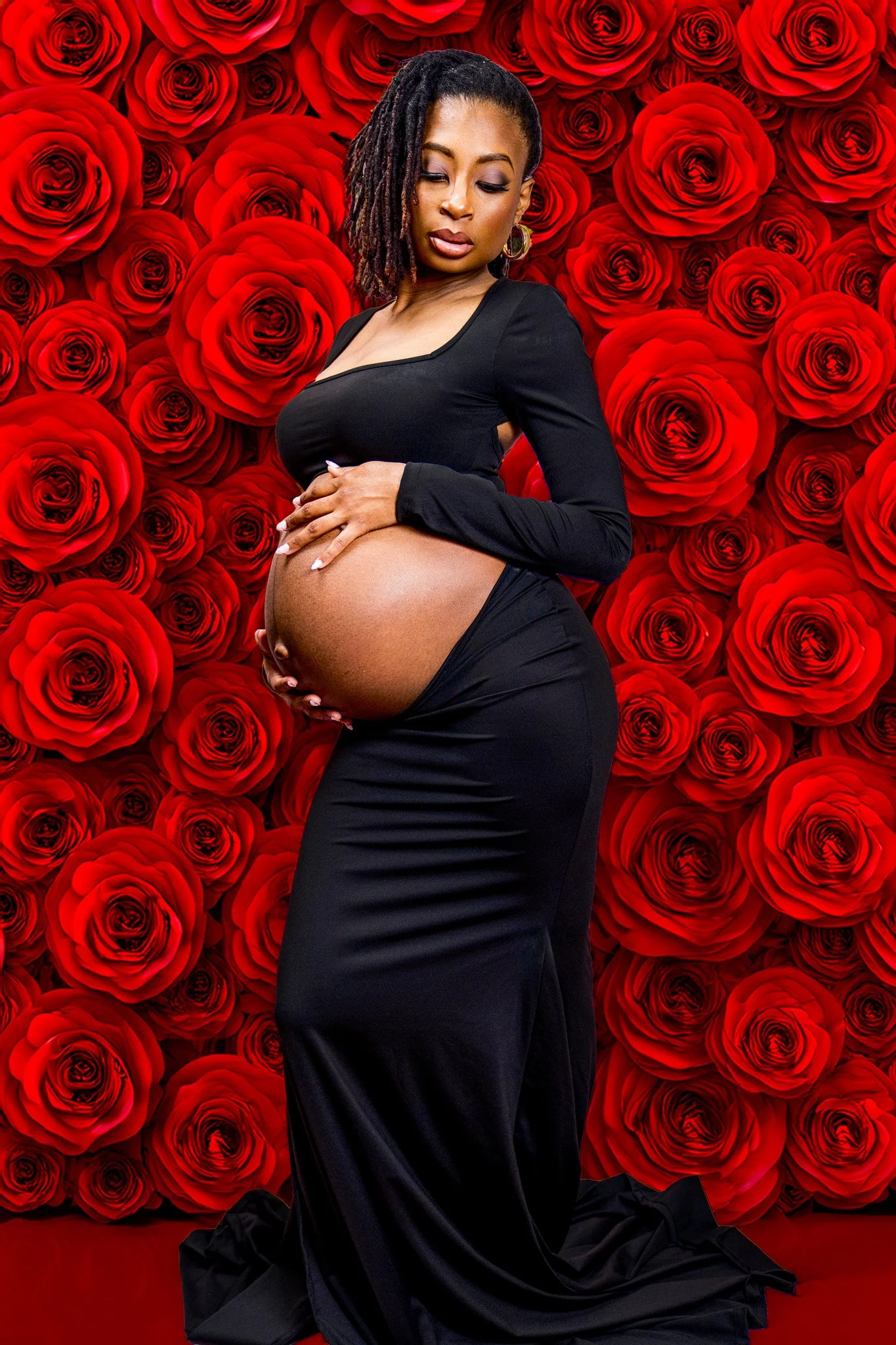 Pregnant woman in a black dress posing in front of a backdrop of red roses.
