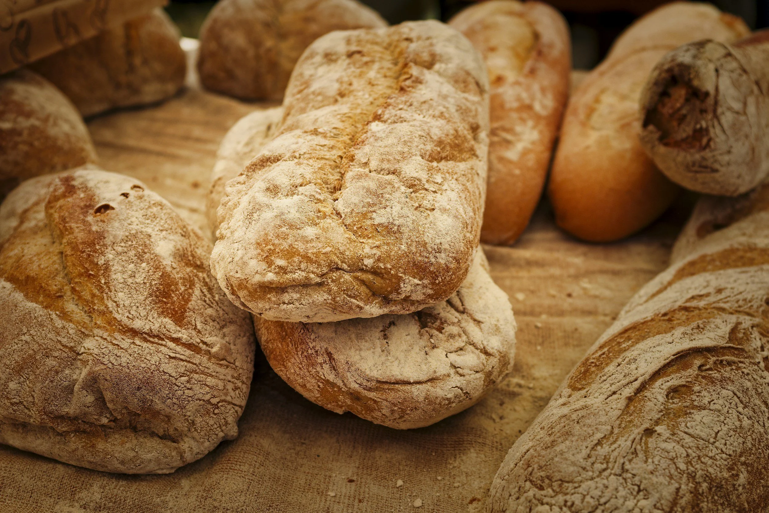 Assorted baguettes and bread rolls dusted with flour arranged on a wooden surface.