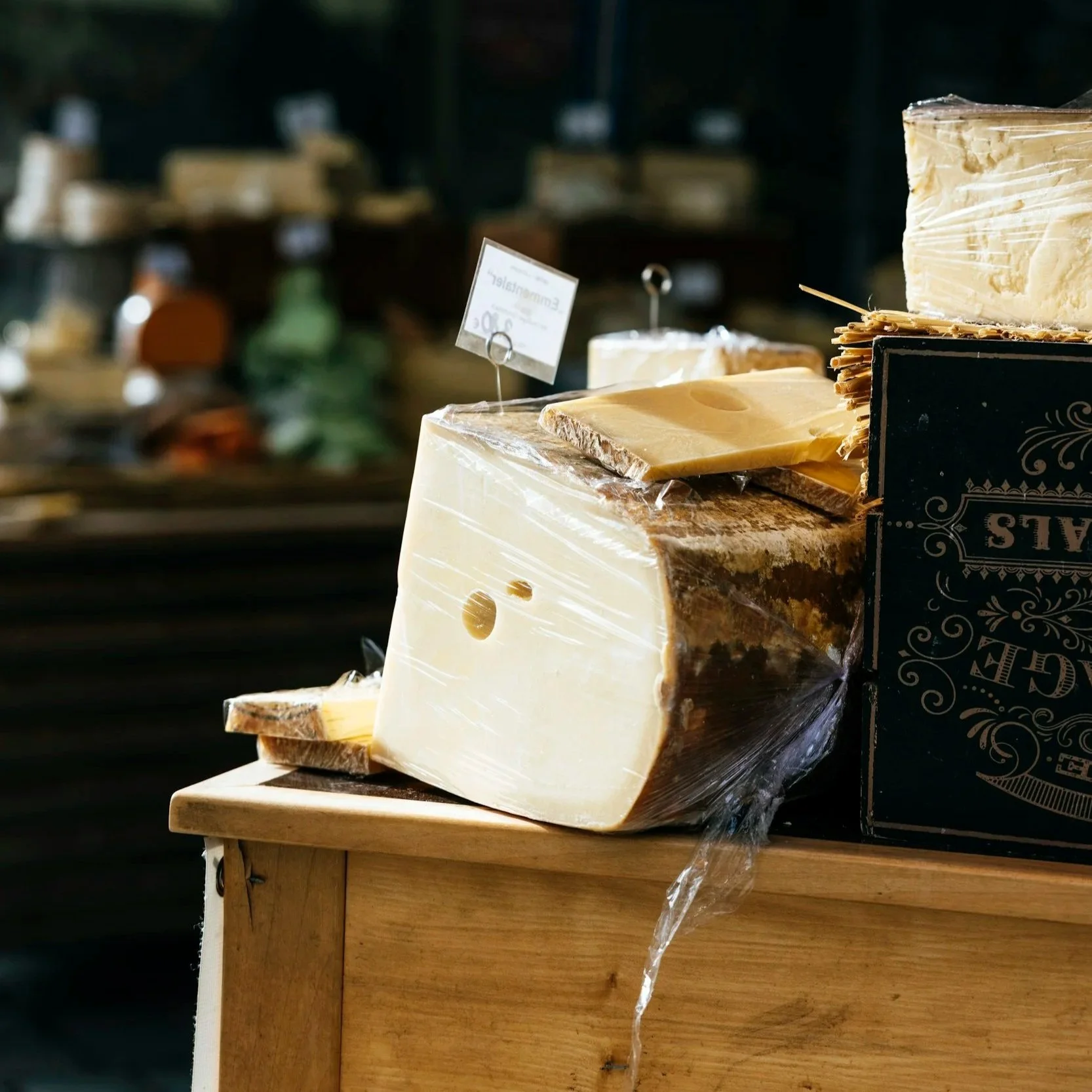 Various types of cheese blocks displayed on a wooden table in a store.