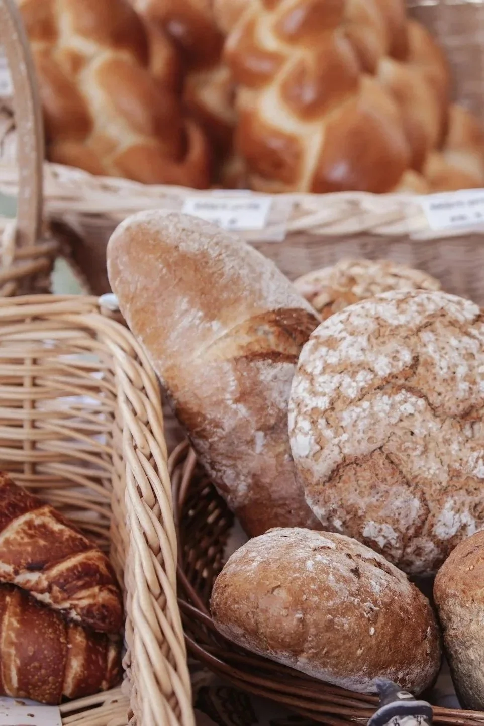 Assorted bakery bread including baguette, rolls, and pretzels in baskets at a bakery.