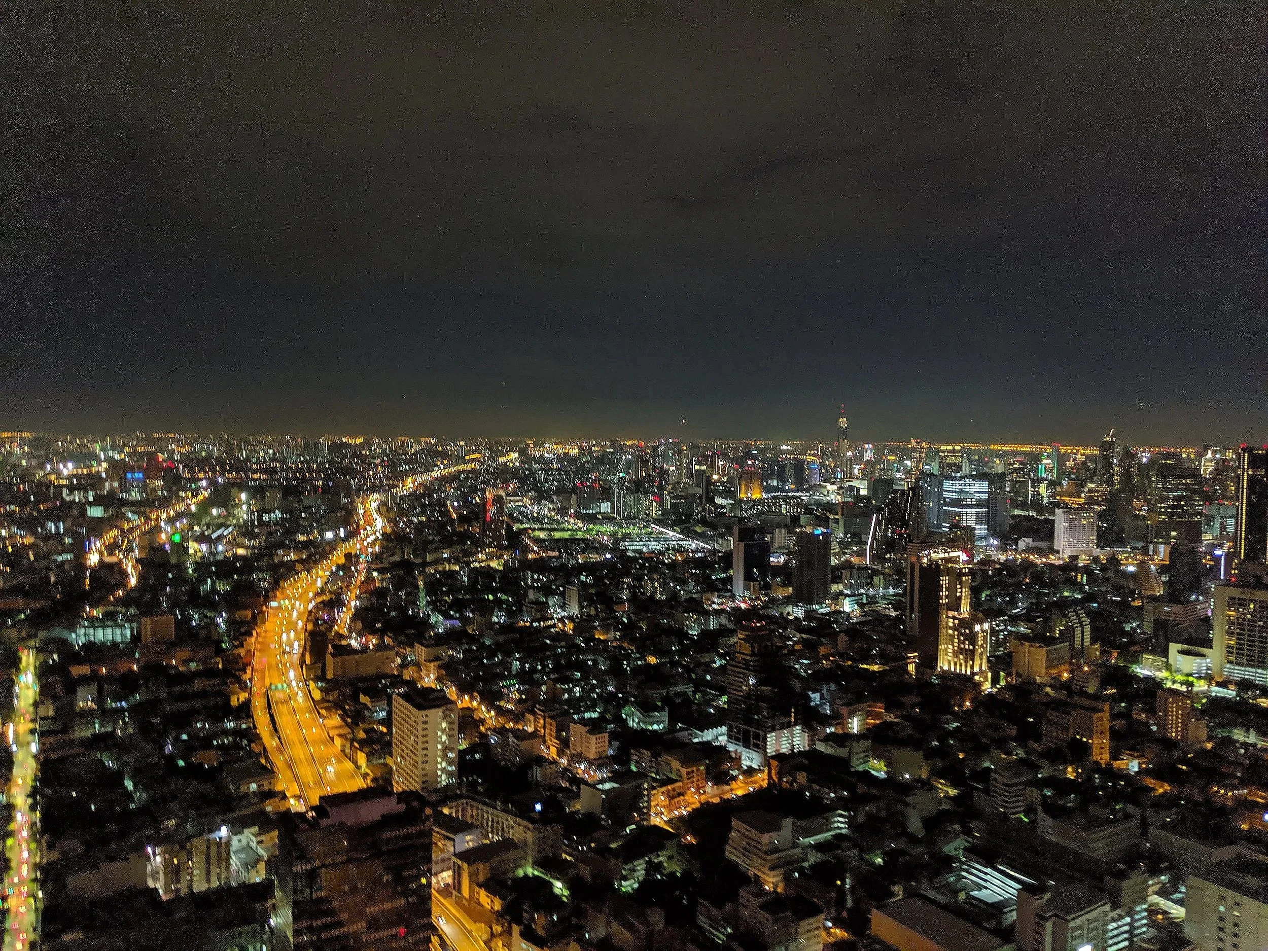 Nighttime cityscape of a dense urban area with illuminated buildings, streets, and lights across the city, with a dark sky overhead.