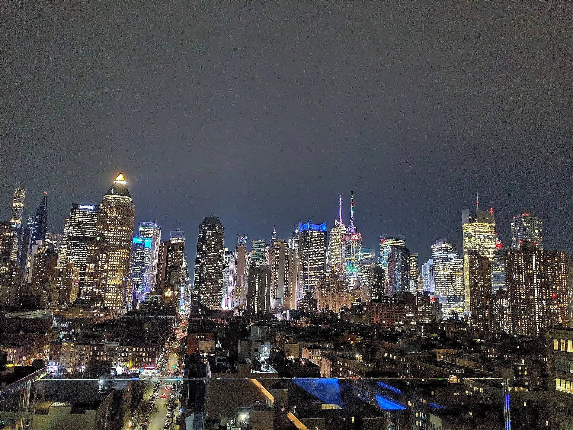 Nighttime city skyline with tall buildings illuminated by colorful lights and a dark cloudy sky.