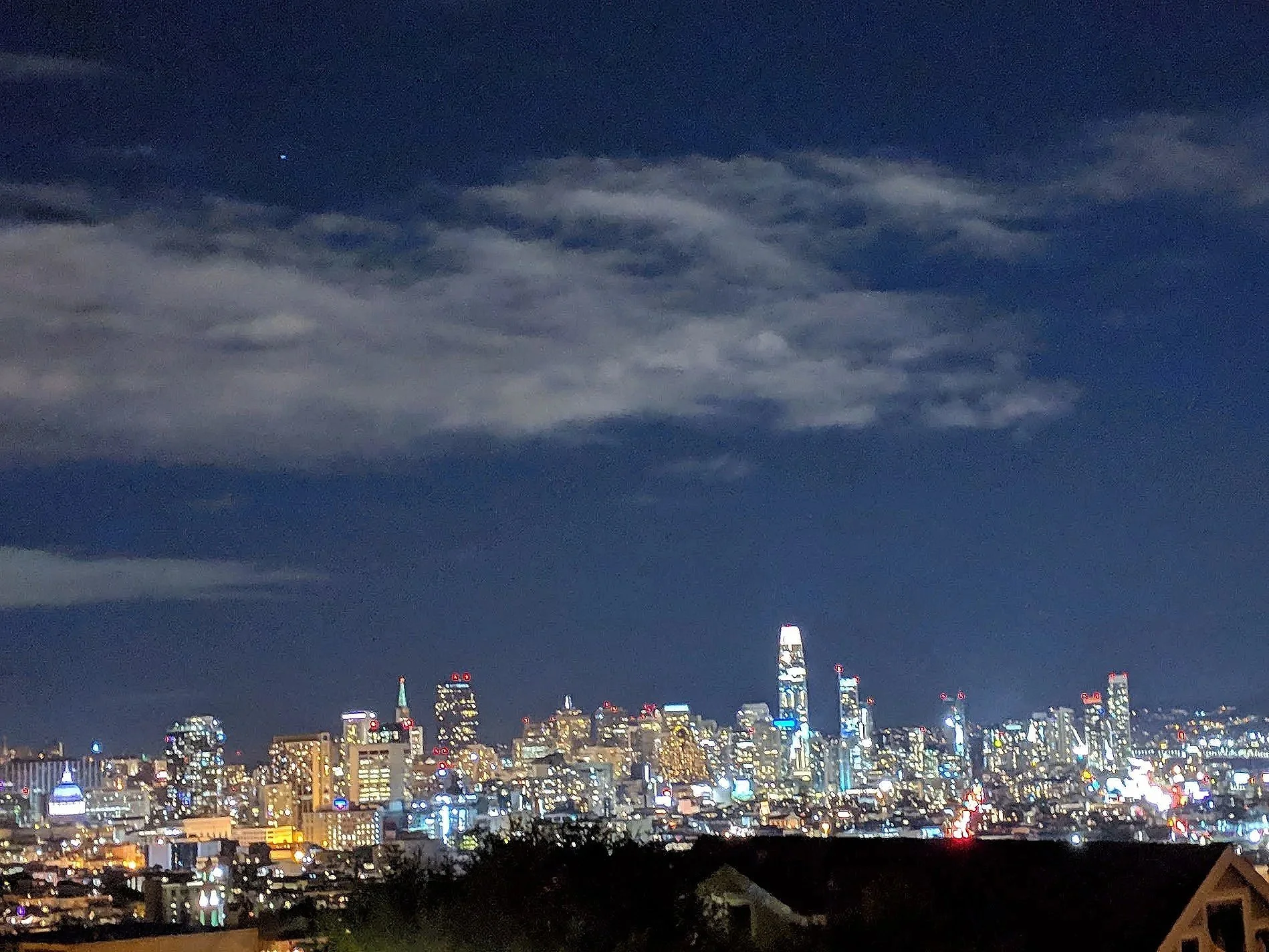 Nighttime cityscape of a downtown area with tall skyscrapers lit up, and a dark cloudy sky overhead with a few visible stars.