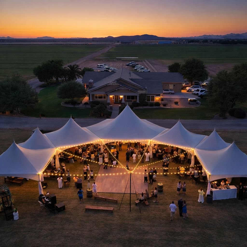 Outdoor wedding reception under a large white tent with string lights, guests mingling, and a backdrop of a rural house and fields at sunset.