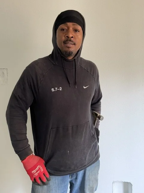 Tall man wearing black sweatshirt and red construction gloves poses for a photo with his hands on his hips
