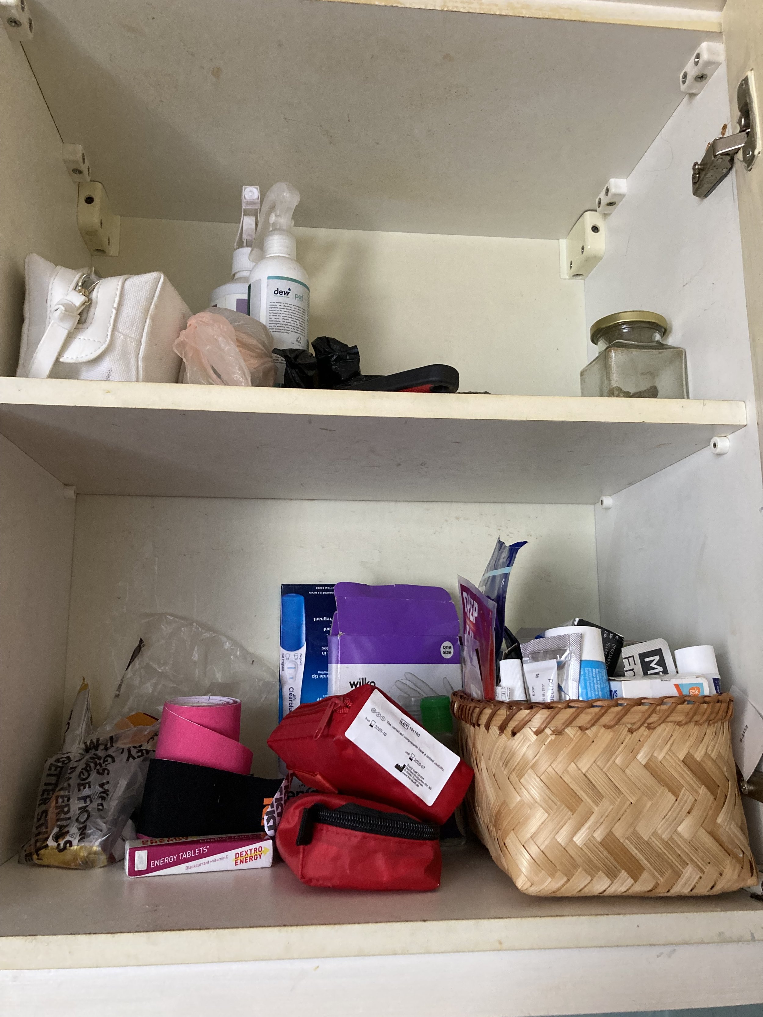 Inside a cabinet, containing miscellaneous items including medicine, first aid supplies, a small woven basket, and various packages and containers.