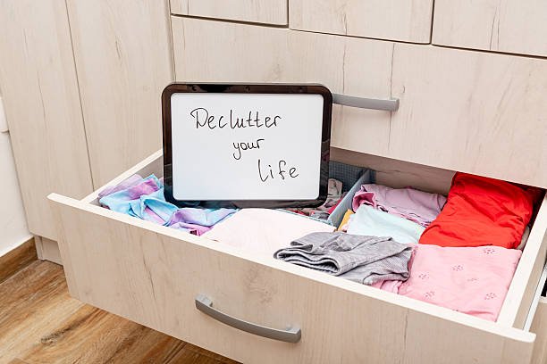 Open drawer filled with folded clothes and a whiteboard with the message 'Declutter your life' written on it.