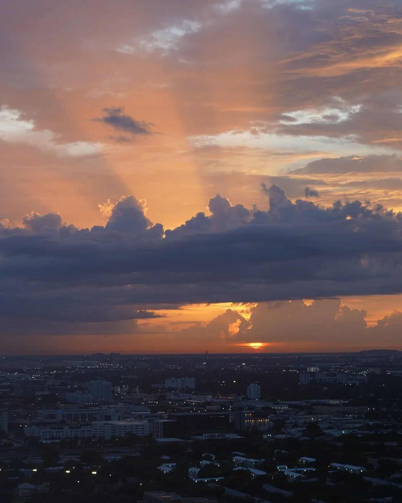 Sunset rays breaking through storm clouds over a city skyline. © Vyretho LLC