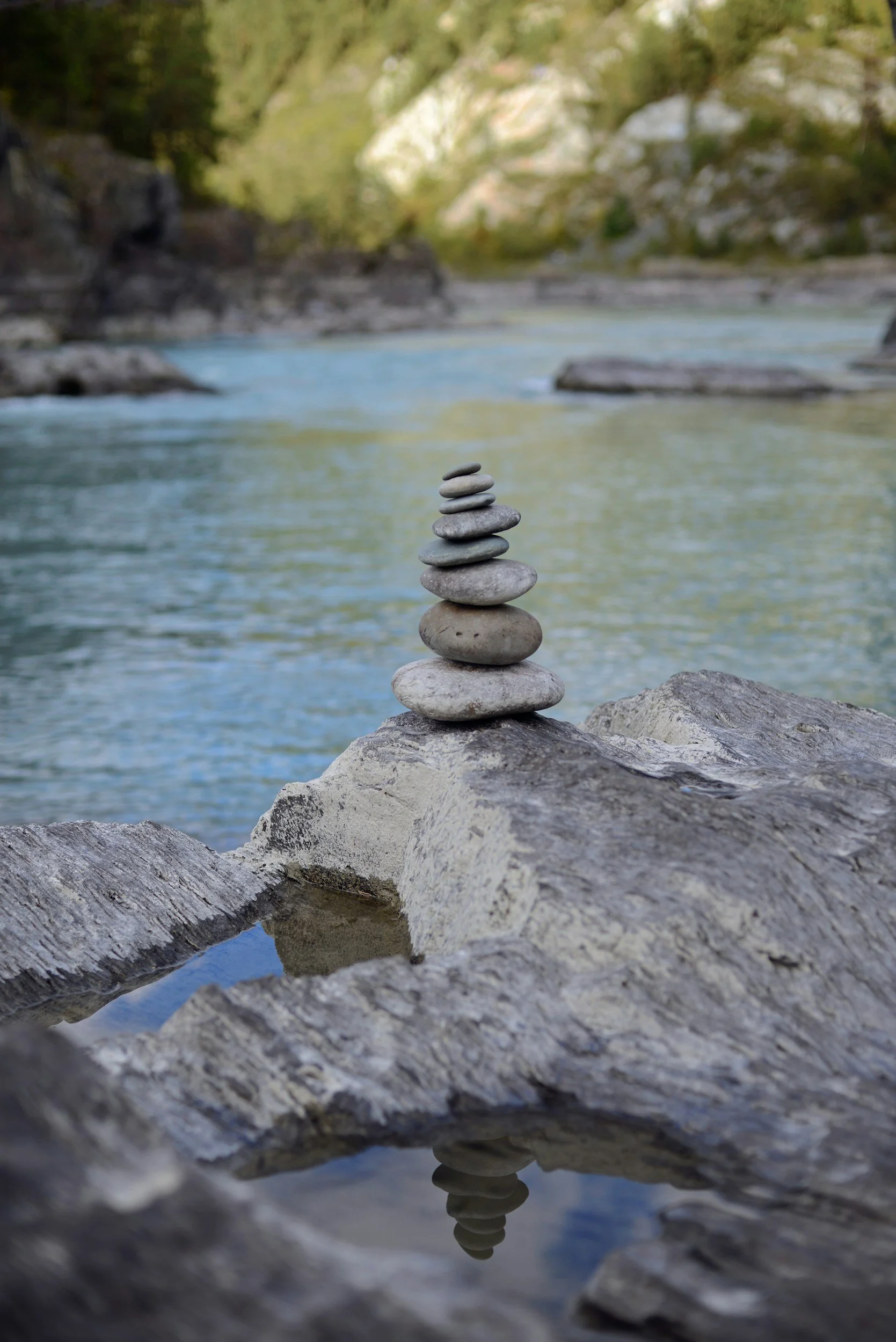 Stack of small, smooth stones balanced on a rock by a river with a forested background.
