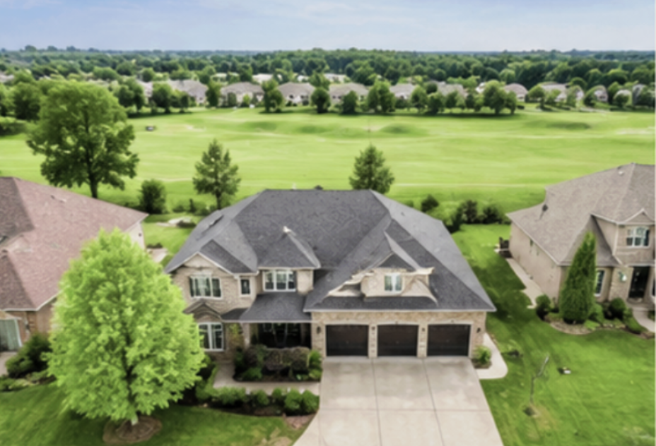 A large suburban house with a three-car garage, surrounded by a well-kept lawn and trees, with a golf course in the background.