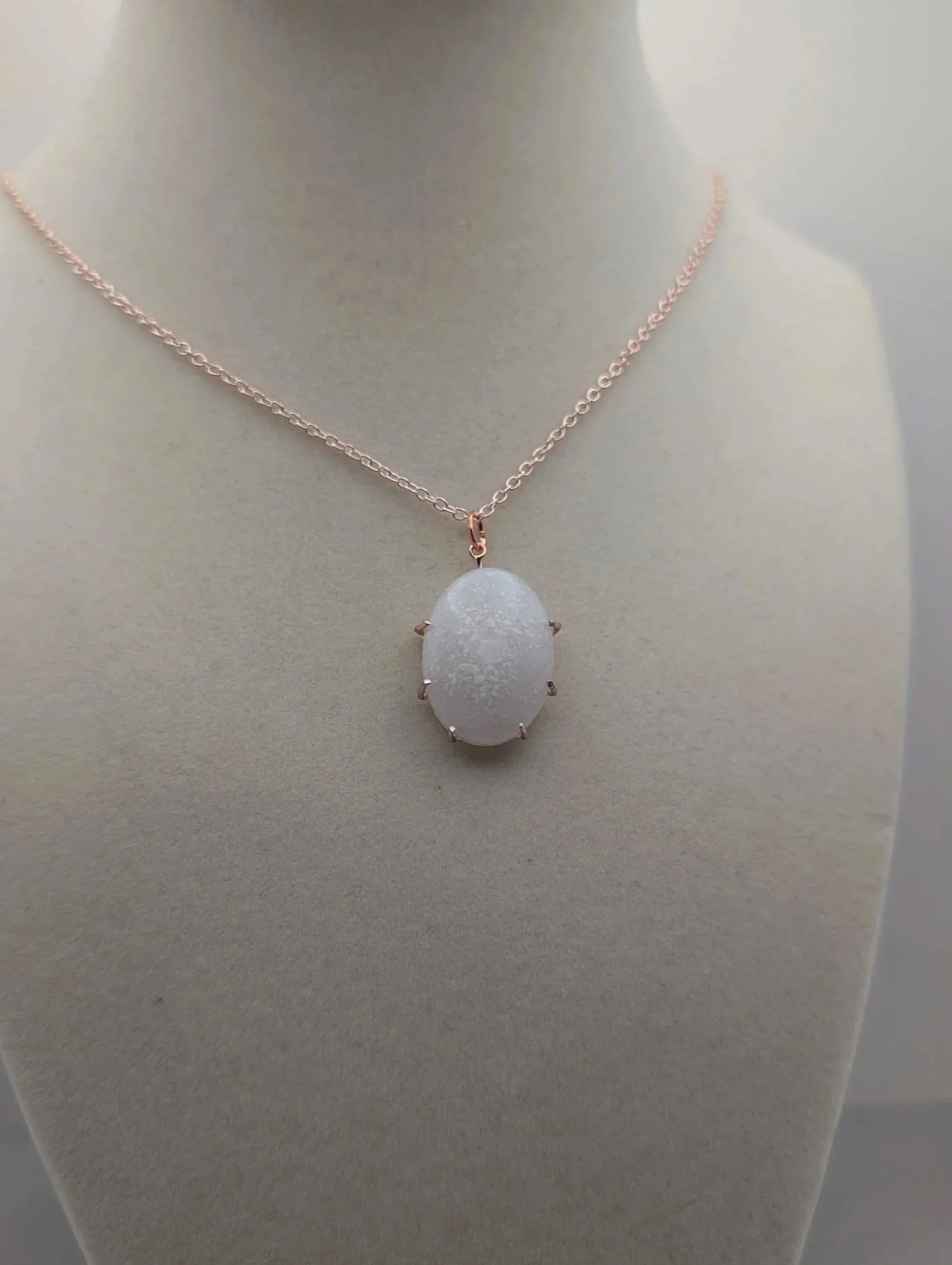 A necklace with a round decorative pendant on a chain, displayed on a white bust form.