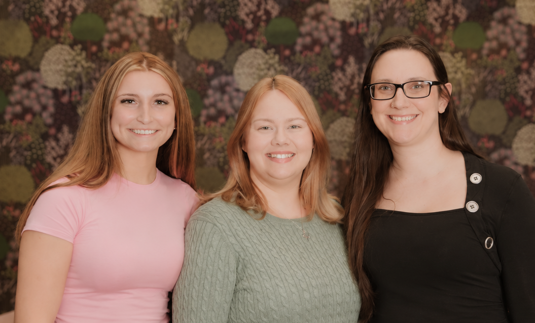 Three women smiling in front of a floral patterned background
