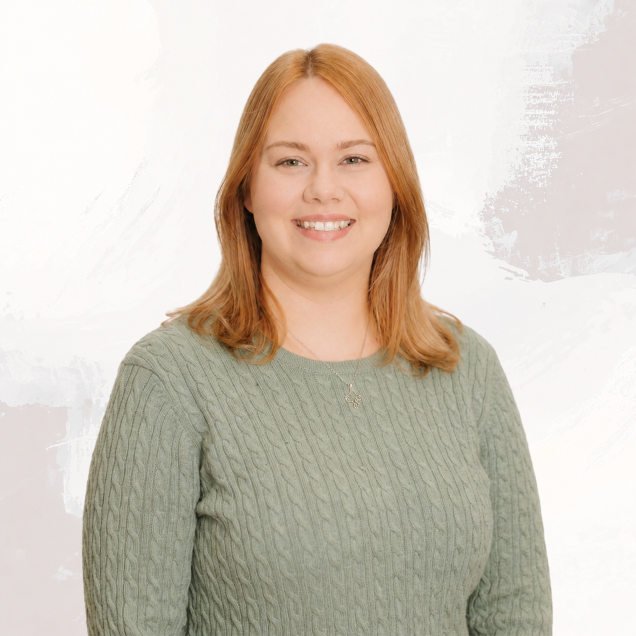 Portrait of a woman with shoulder-length red hair, wearing a green cable-knit sweater and a delicate necklace, smiling against a plain white background.