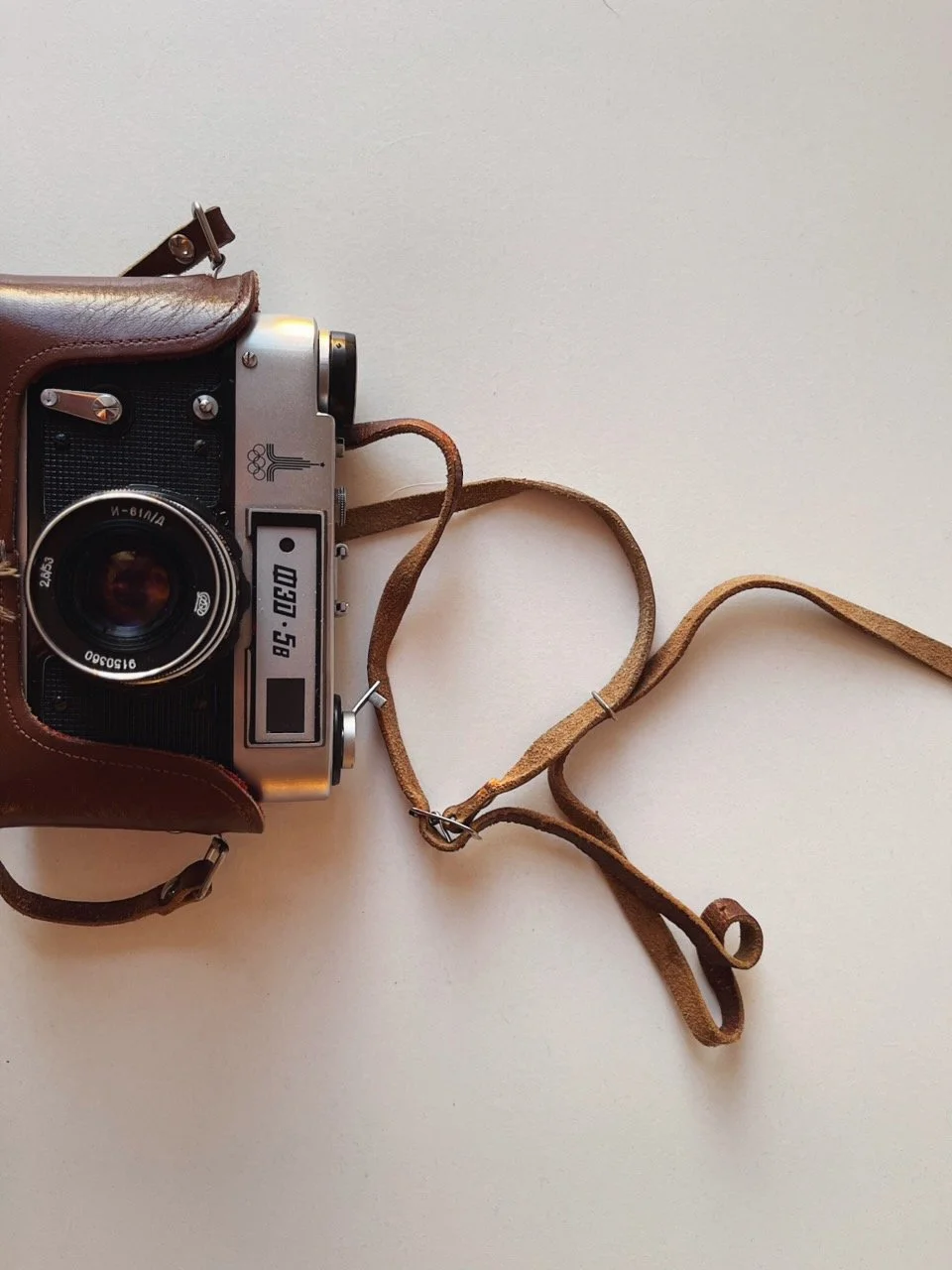 A vintage film camera with a leather strap on a white surface.