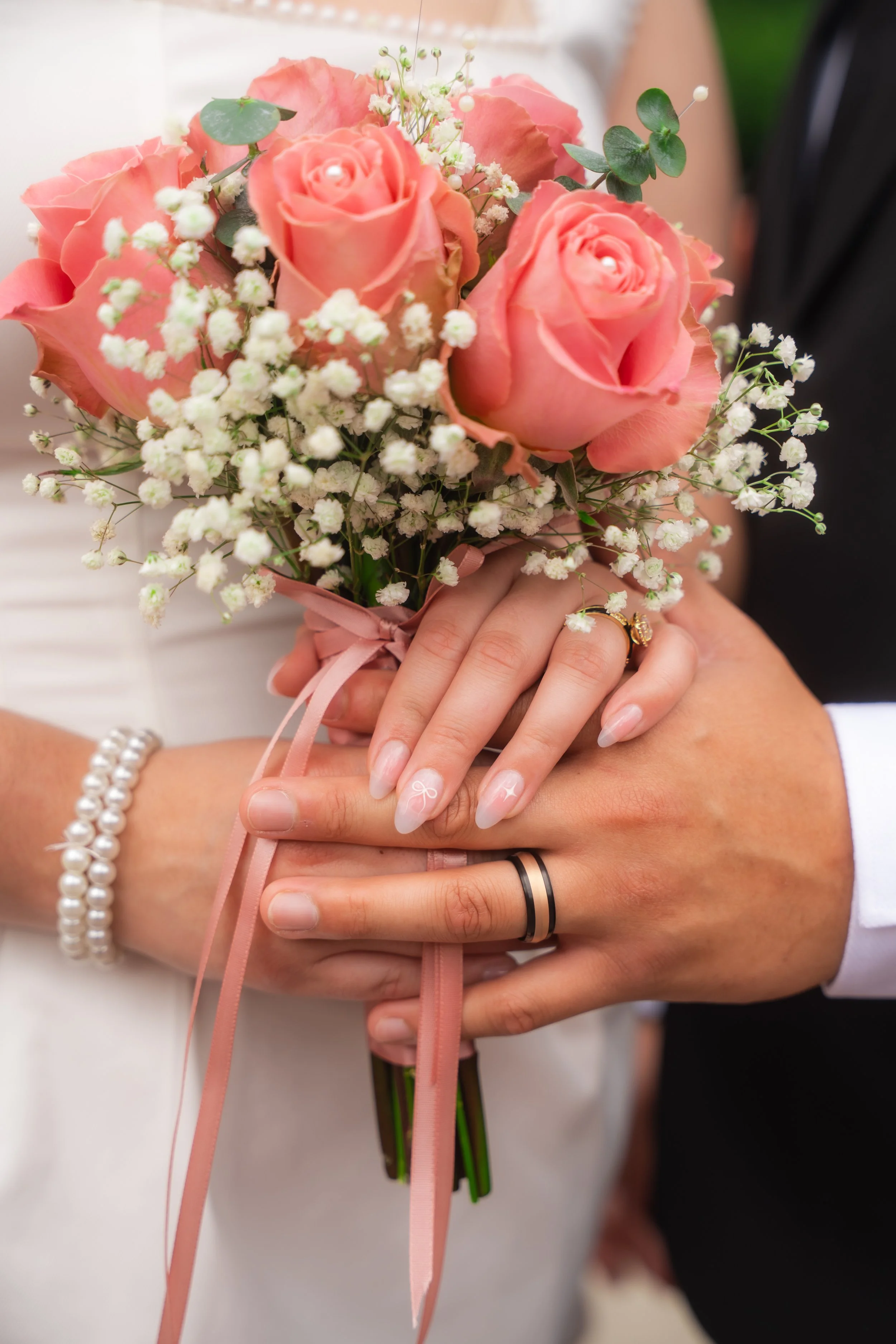 Close-up of a person holding a bouquet of pink roses, baby's breath, and greenery, tied with pink ribbon.