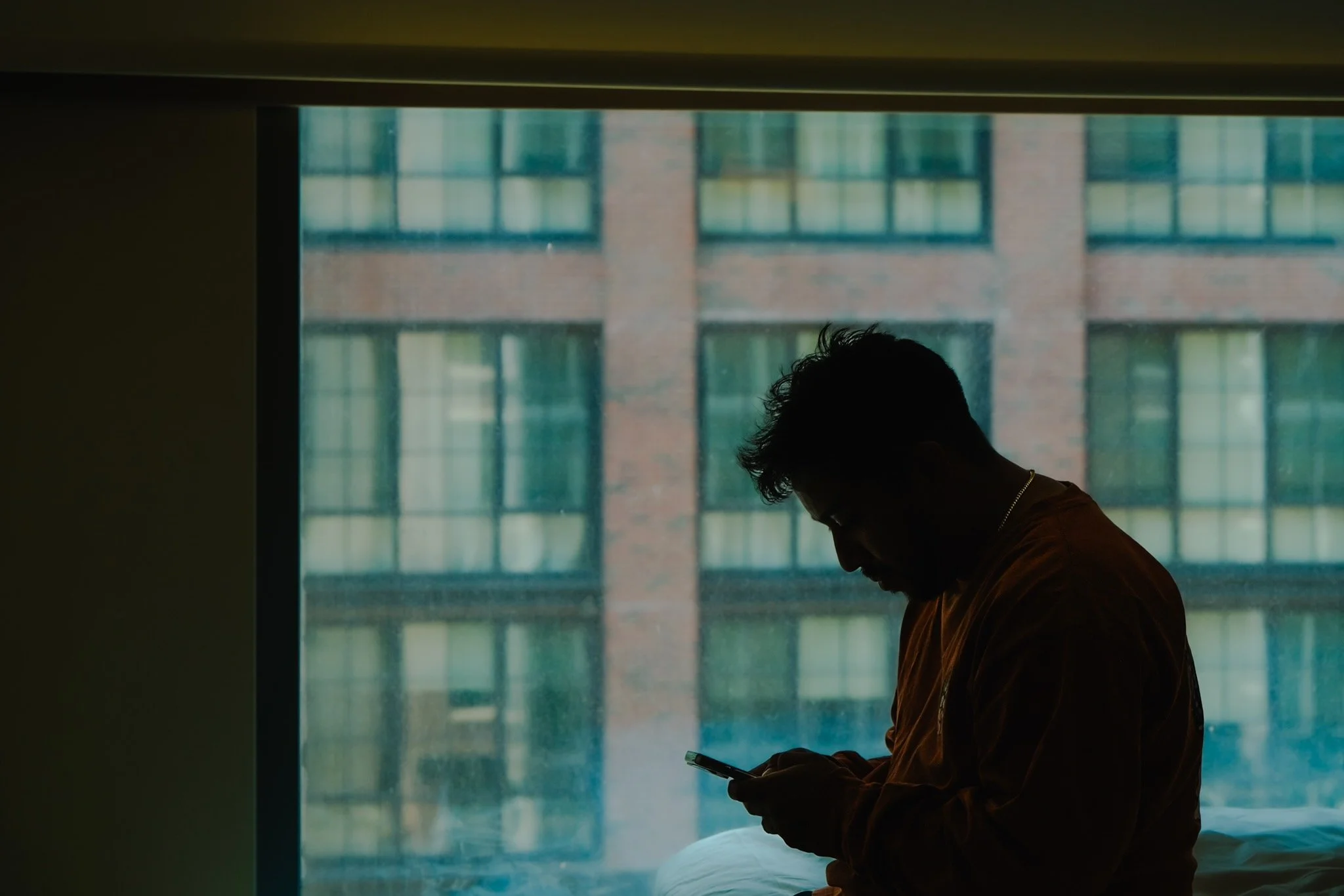 Person sitting near window looking at a mobile phone during daytime.