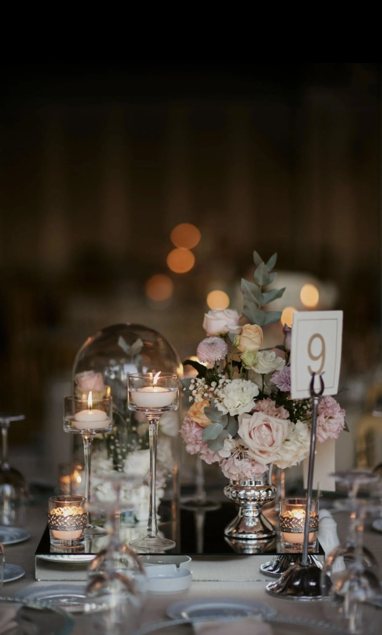 Elegant table setting with floral centerpiece, candles, and a table number card at an event or wedding reception.