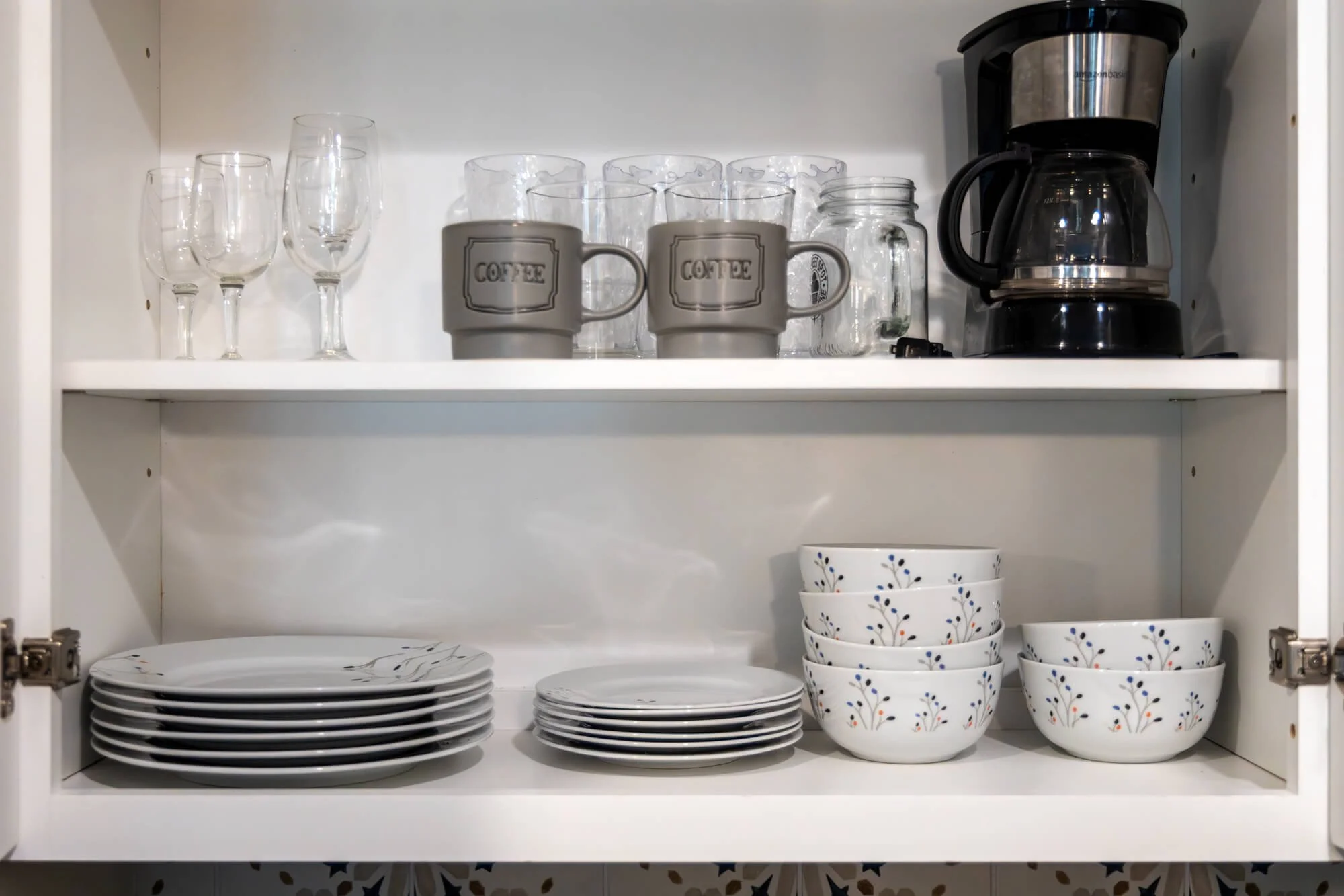 Stocked kitchen cabinet with dishware, glassware, and coffee maker