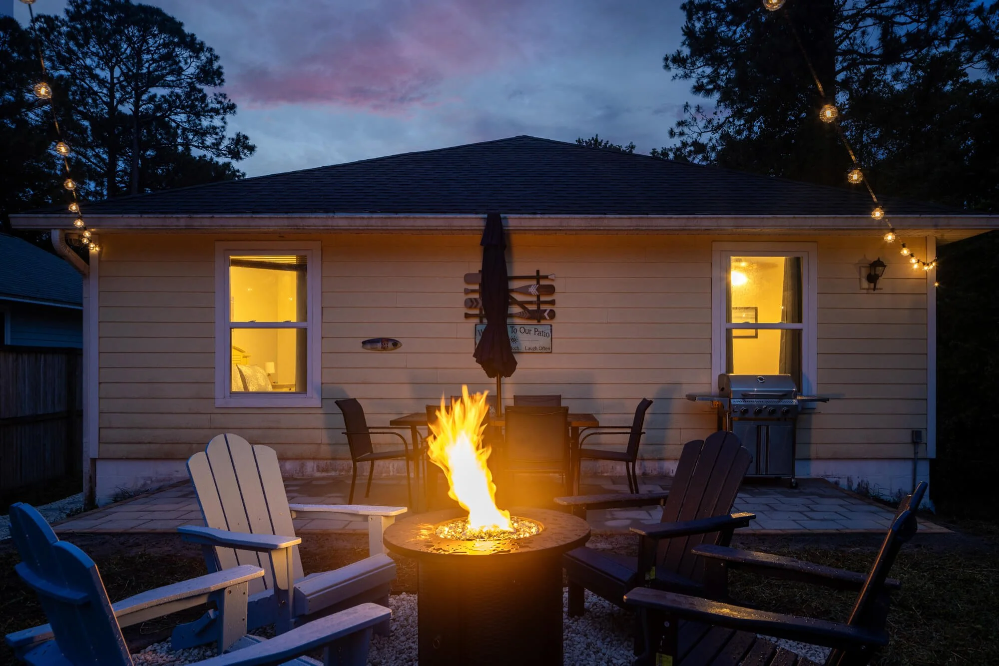 Backyard fire pit with Adirondack chairs and string lights at dusk