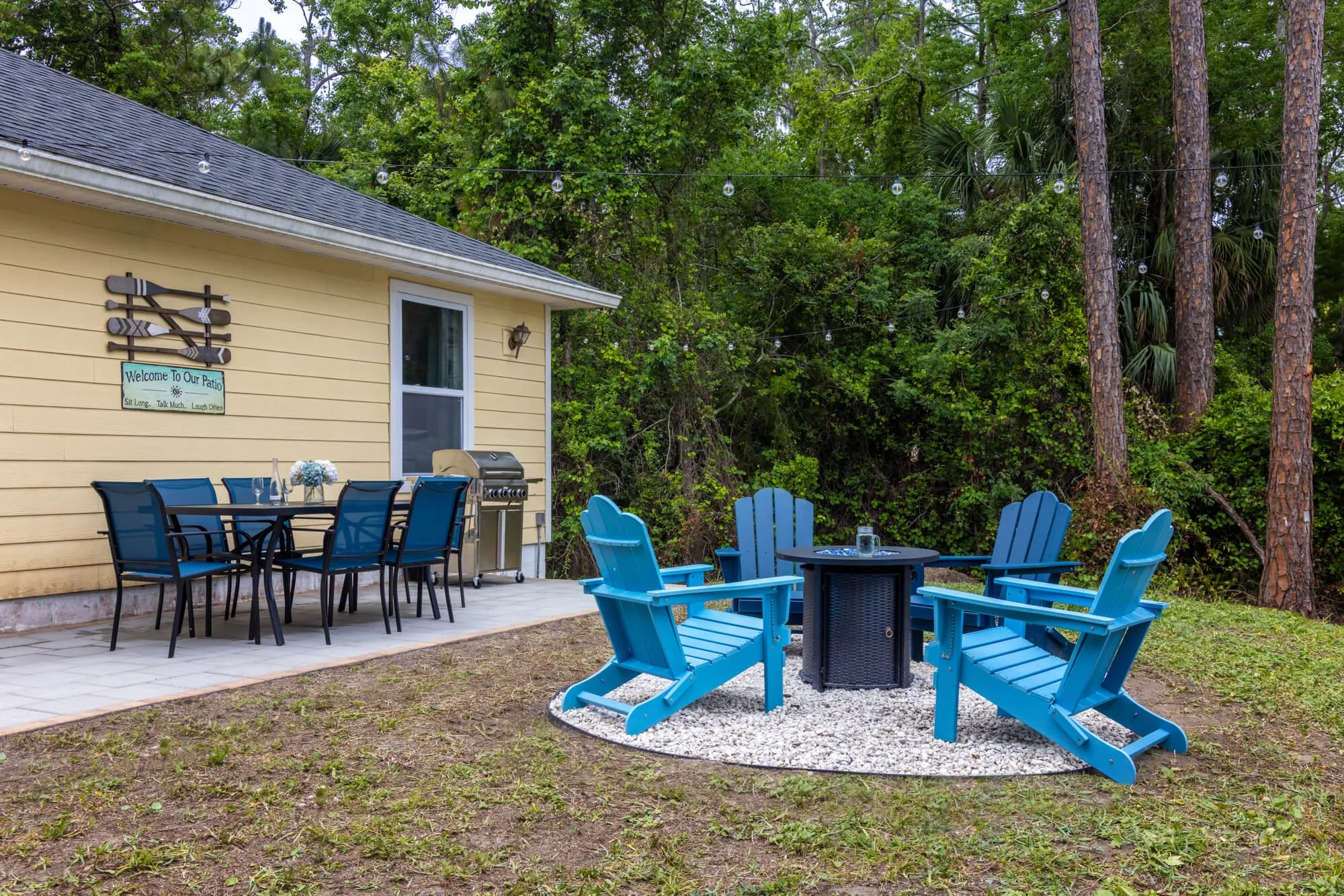 Backyard patio with fire pit, dining area, grill, and string lights