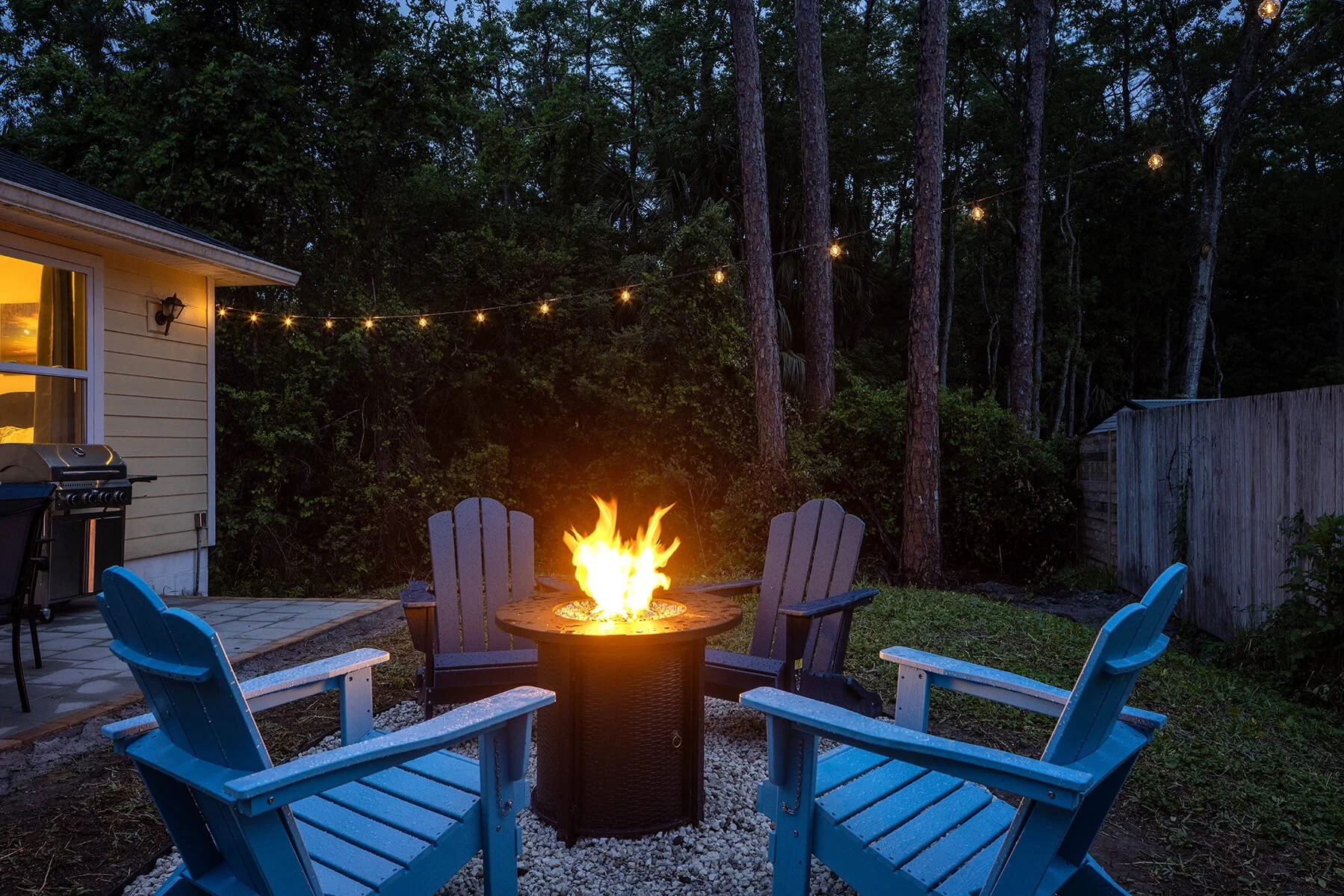 Backyard fire pit with Adirondack chairs and string lights at dusk