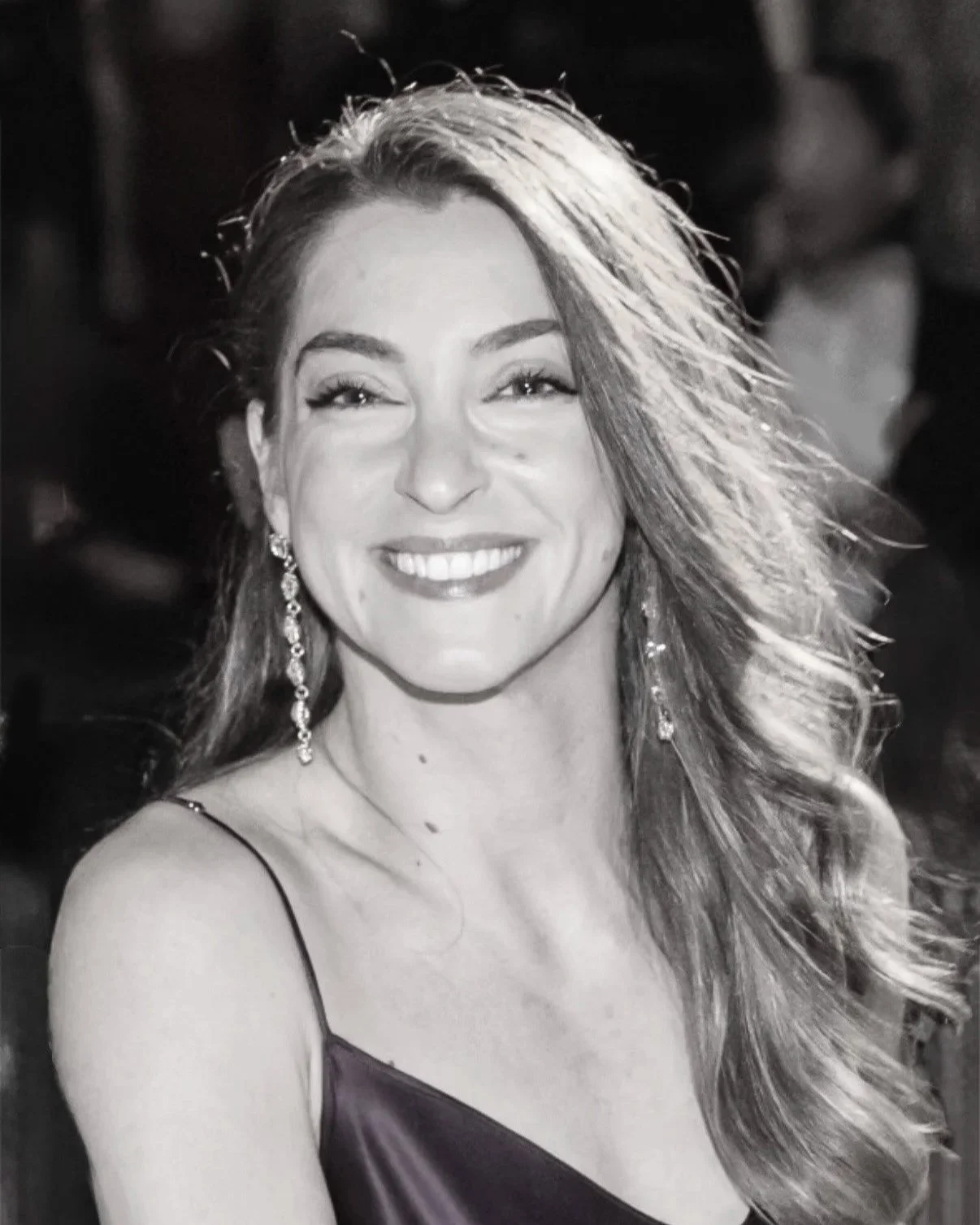 A smiling woman with wavy hair wearing earrings, a spaghetti strap top, and looking at the camera.