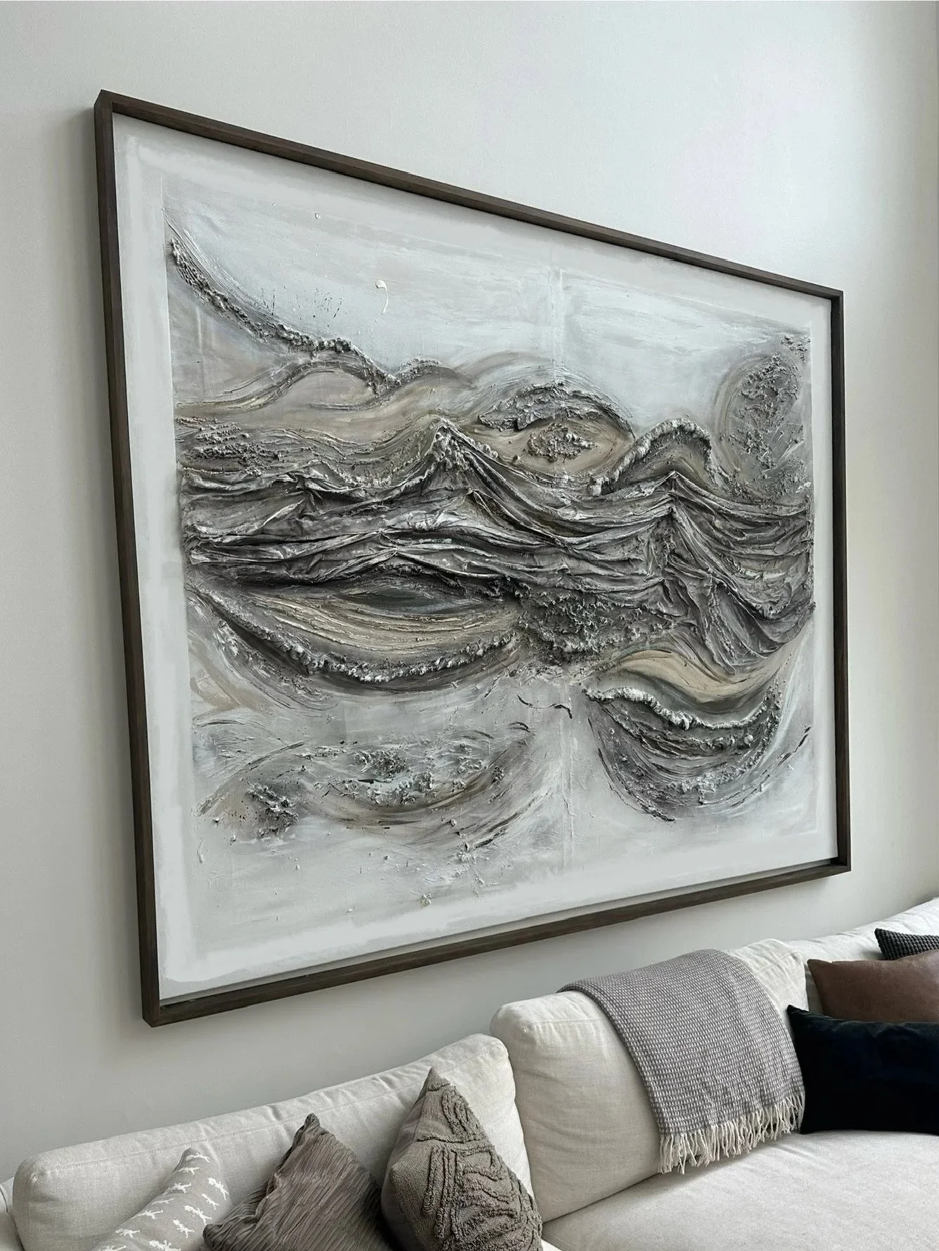 Large abstract textured painting with swirling patterns in shades of gray, black, and white hanging above a white sofa in a modern living room.