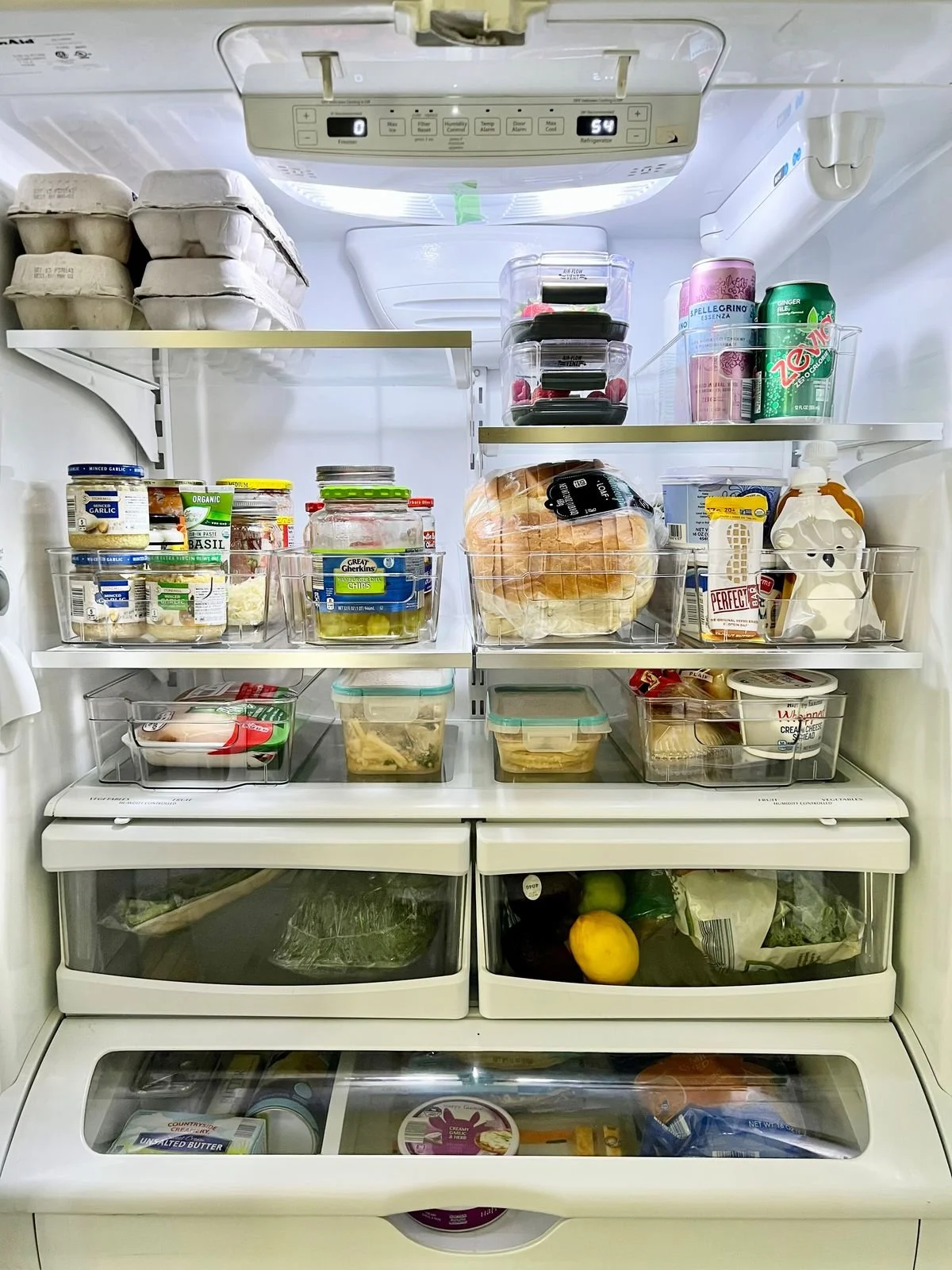 Inside of a refrigerator filled with various food and beverage items, including eggs, containers, bread, dairy products, fruits, and packaged foods.